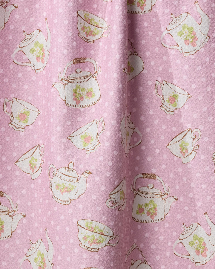 Strawberry Tea by Geometry features pink fabric with white polka dots and vintage teapots, teacups, and saucers adorned with green leaves and pink roses—ideal for a charming kitchen towel.