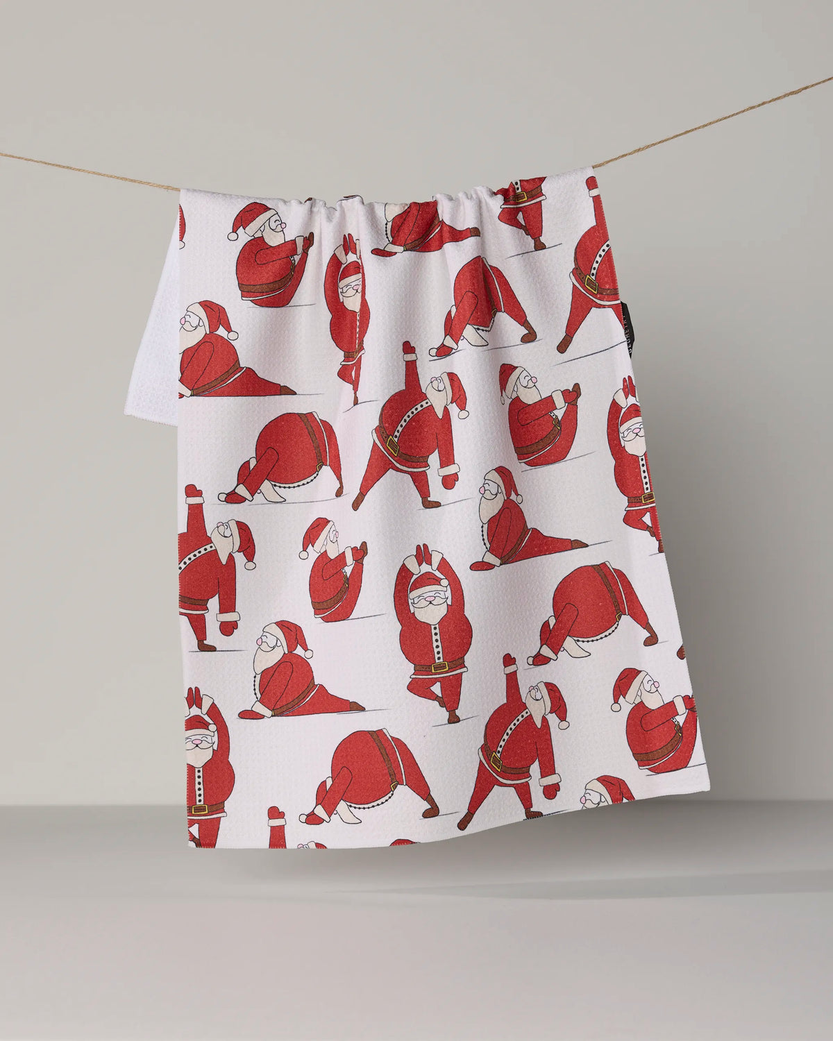 The Geometry “Stretchy Santy” tea towel features playful red illustrations of Santa Claus in different yoga poses on a crisp white background. This eco-friendly, absorbent dish towel adds a festive touch to your kitchen while supporting sustainable choices for the holiday season.