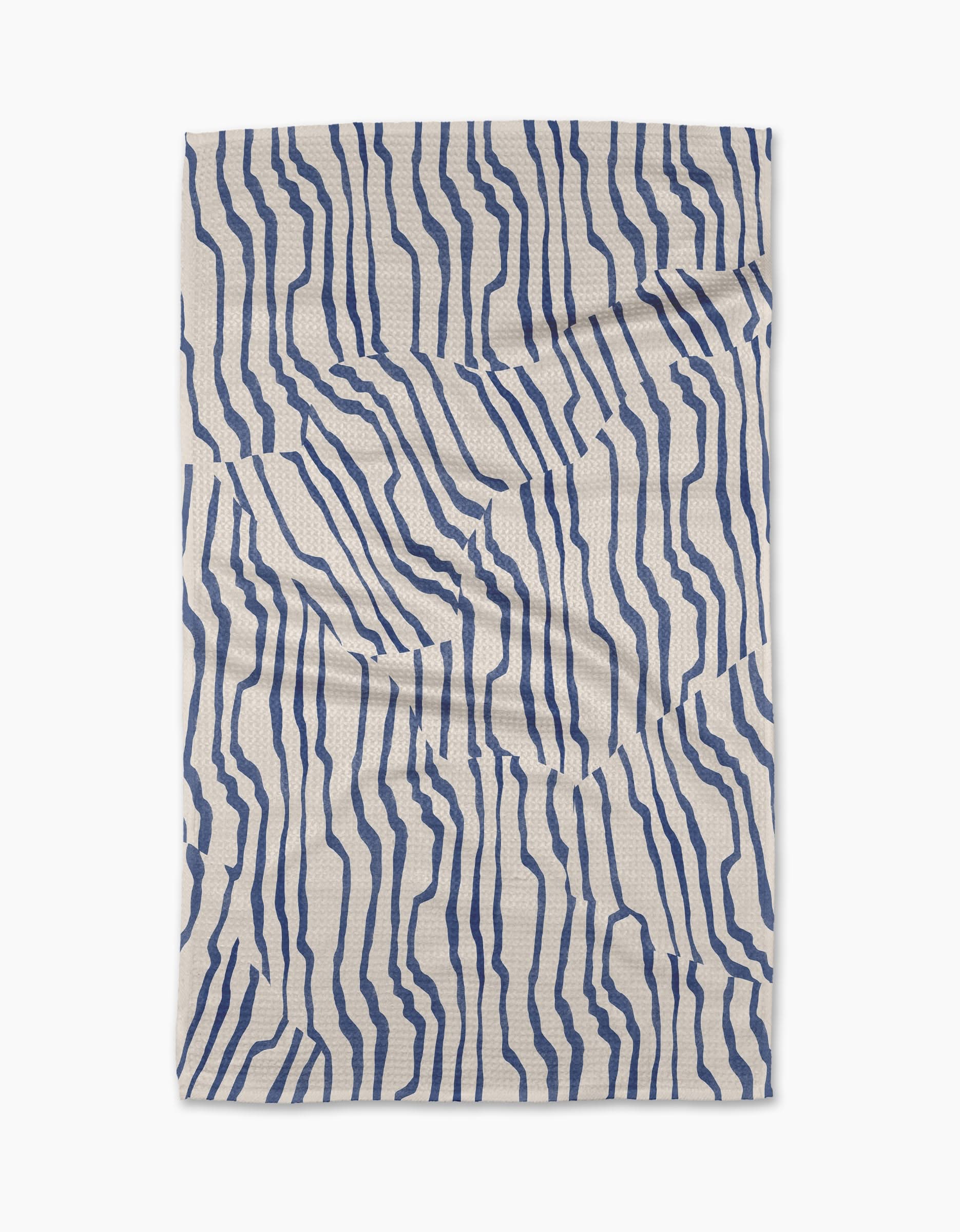 The Geometry Stripe Funk Grounds Blue is a rectangular beige tea towel made from recycled materials, featuring irregular wavy navy blue lines in an abstract, organic pattern on its slightly wrinkled surface.