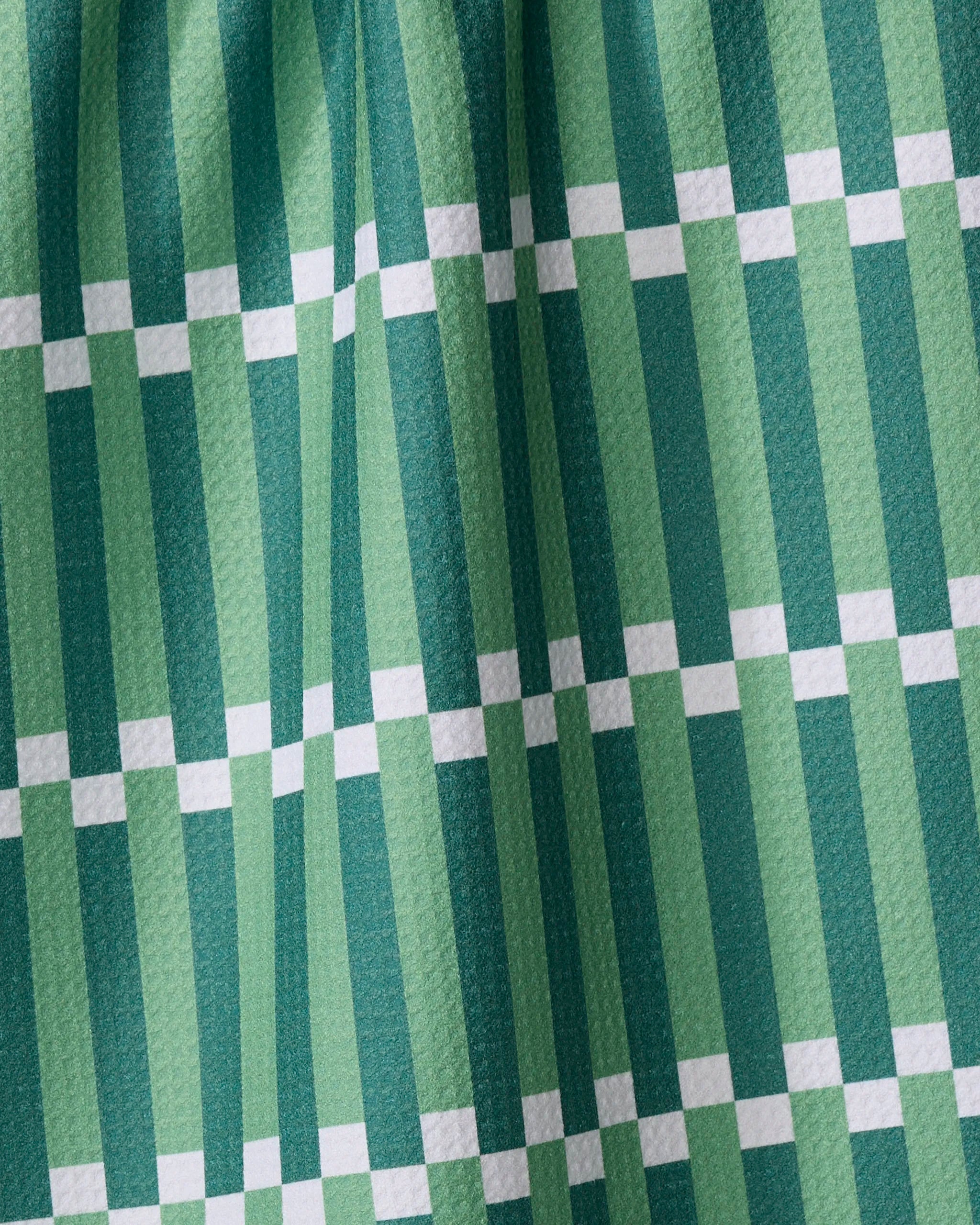 The Buy Guide's Stripe Block - Greens tea towel features a green and white checkered pattern with alternating dark and light green stripes crossed by horizontal white lines.