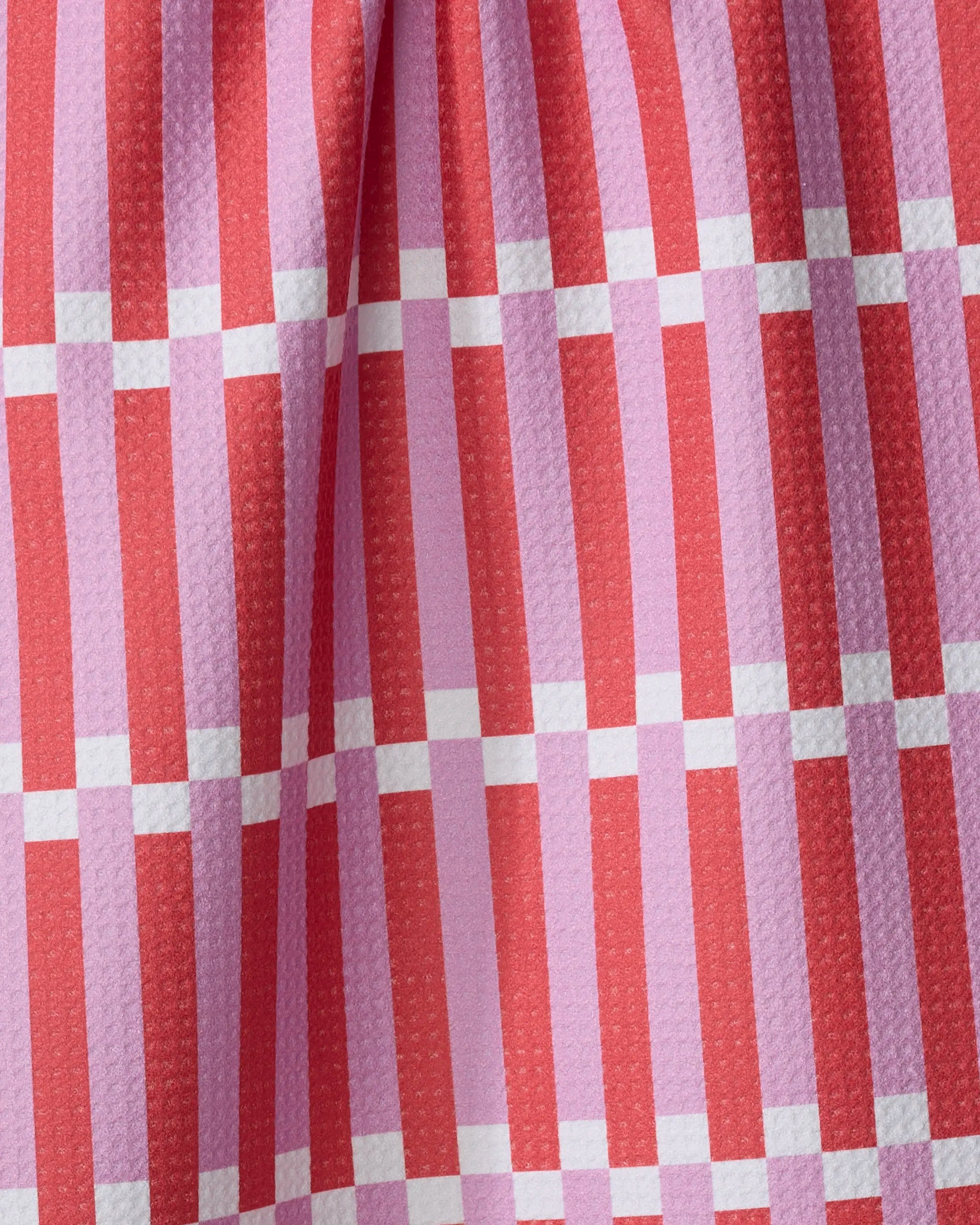 A close-up of The Buy Guide's Stripe Block - Pink Red fabric shows a textured, slightly pleated surface with red vertical stripes, pink horizontal stripes, and thin white lines forming a classic checkered tea towel pattern.