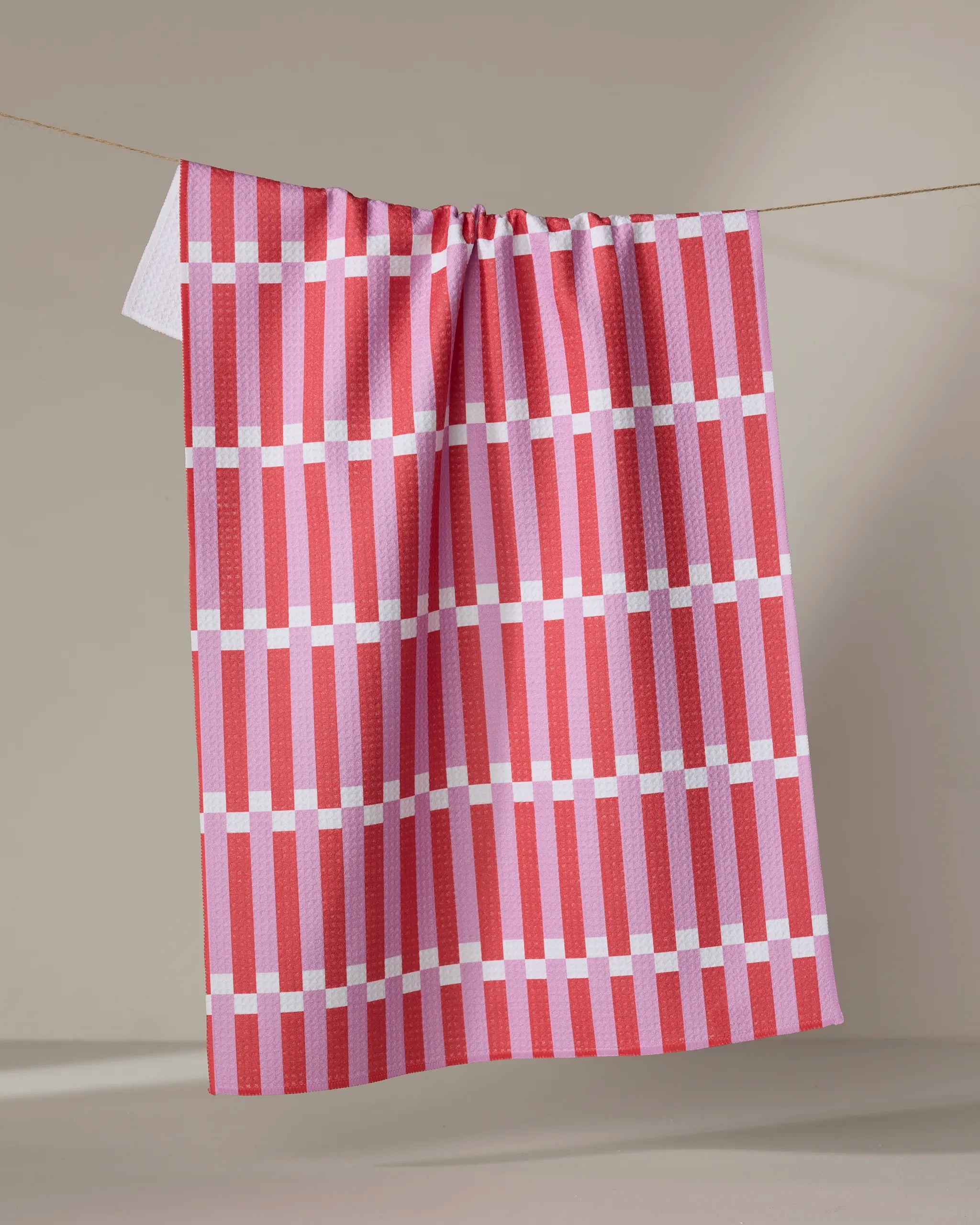 The Buy Guide’s Stripe Block - Pink Red dish towel, featuring a red, pink, and white plaid pattern, hangs neatly on a clothesline against a neutral background.
