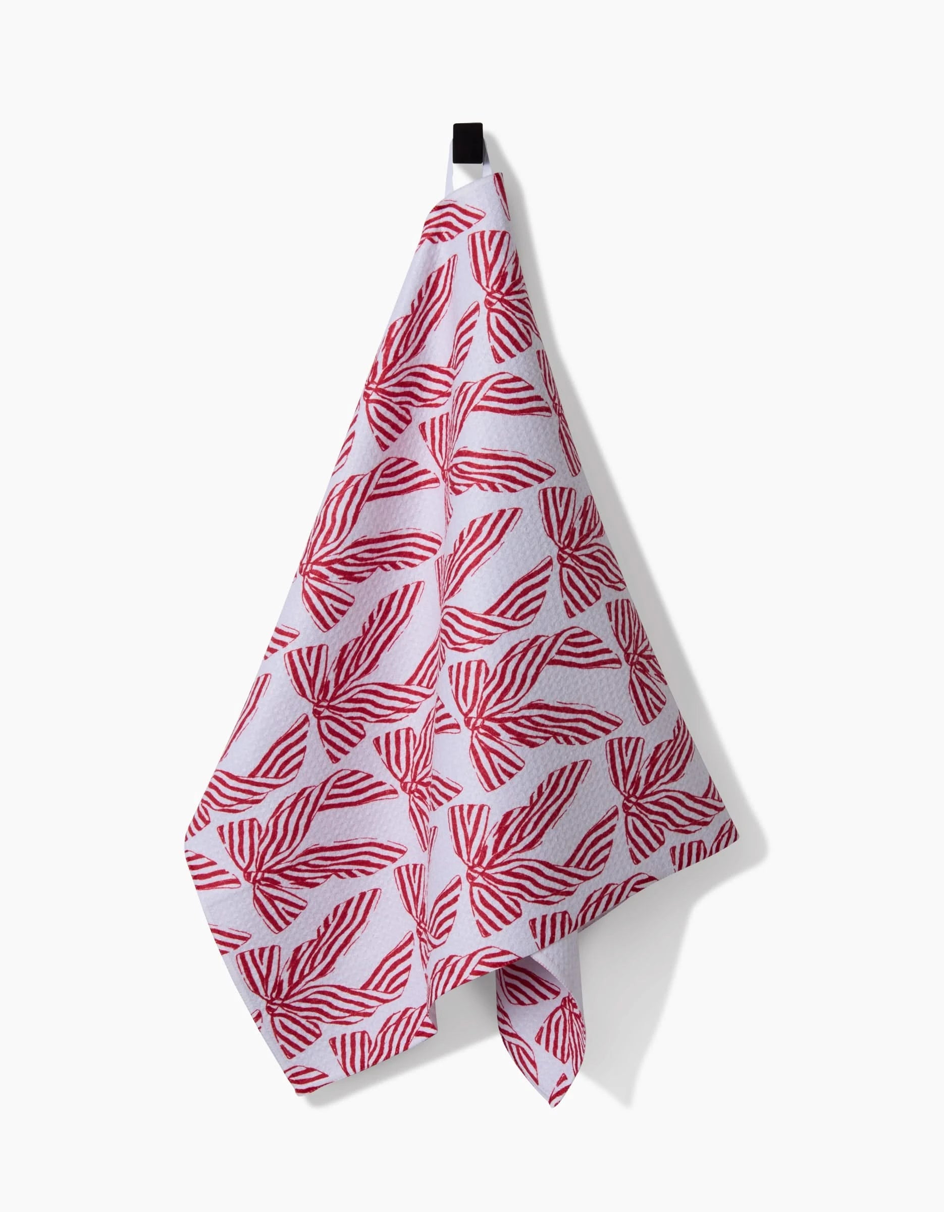 A Hufton Studio Striped Bows kitchen towel with red leaf-like geometric patterns hangs from a black hook against a plain white background.