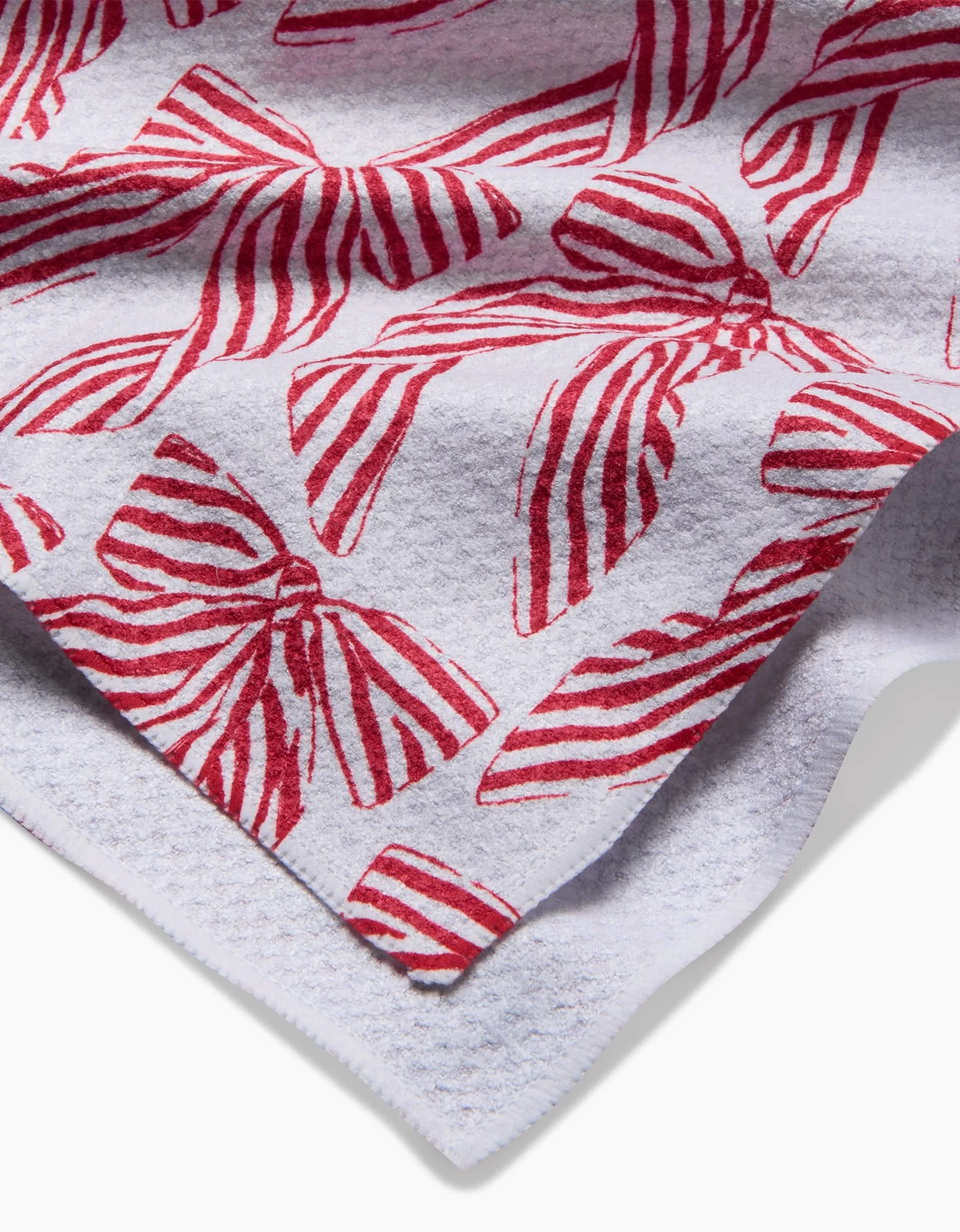 A close-up of Hufton Studio’s Striped Bows tea towel shows its white textured fabric and printed red, striped bows pattern, with gentle folds highlighting the design and texture.