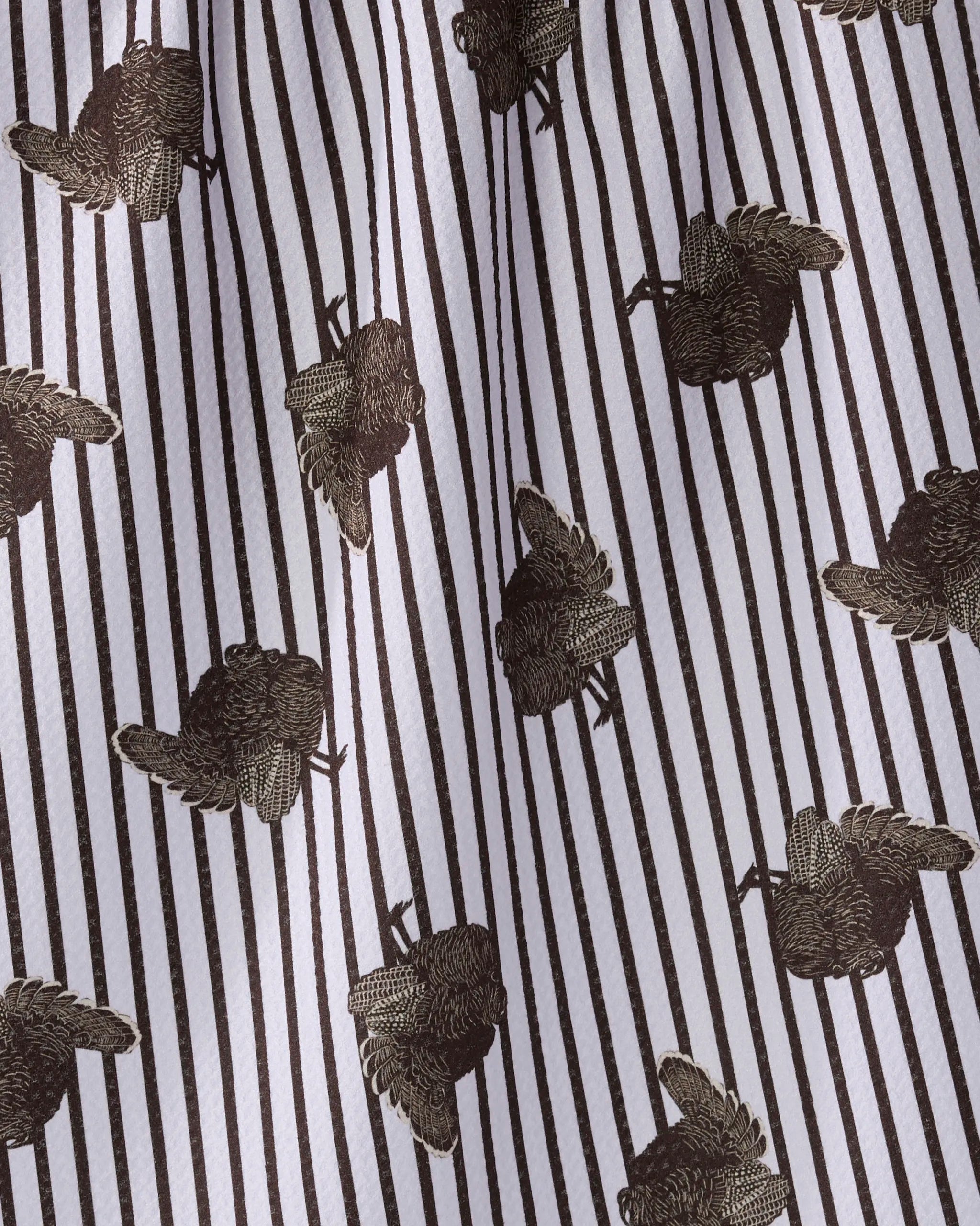 The Geometry Strut tea towel features vertical black stripes and embroidered brown bird motifs with the letter K on soft, recycled white fabric that drapes gracefully.
