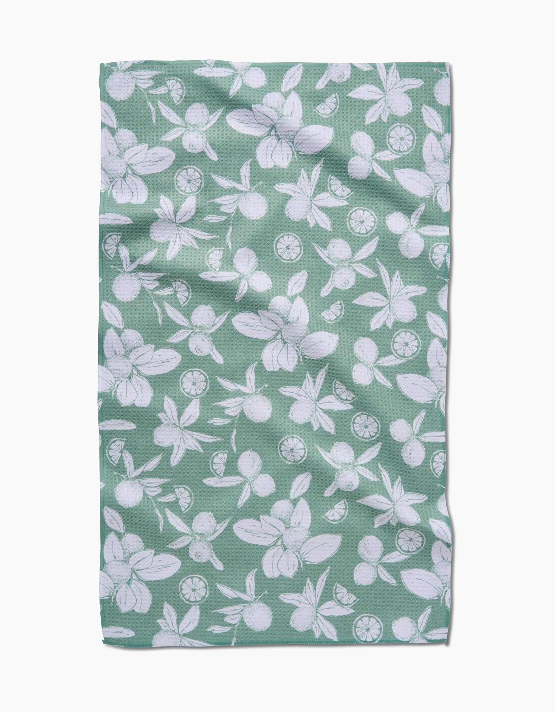 A green rectangular Summer Limes tea towel by Hufton Studio, made from recycled materials, features a white floral and citrus fruit pattern and is shown flat with slight wrinkles.
