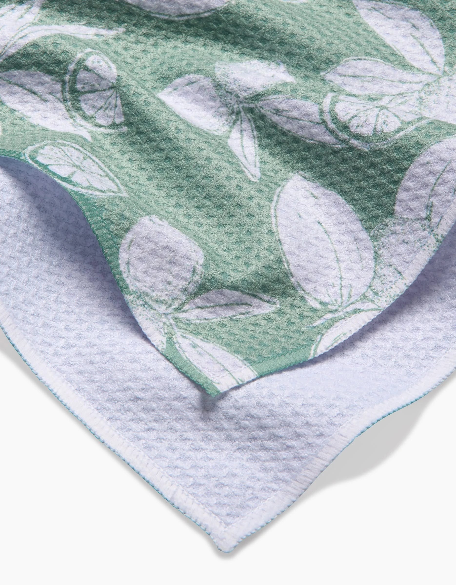 A close-up of a textured green and white Hufton Studio Summer Limes Tea Towel, showing a leafy botanical pattern on one side and plain white Geoweave fabric on the reverse.