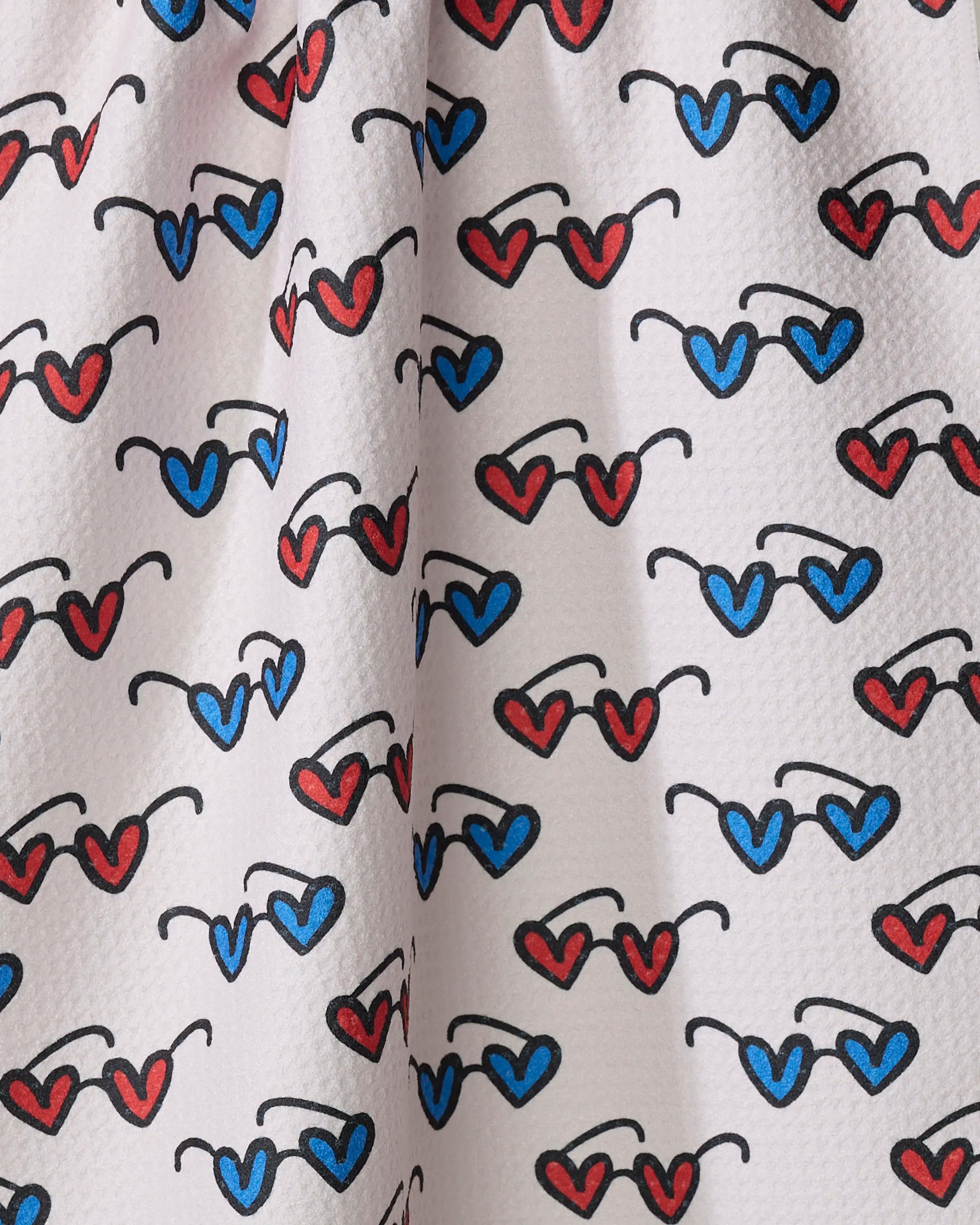 The Kayla Ann "Summer Sunglasses" towel is white, quick-drying, and features diagonal rows of red and blue heart-shaped sunglasses with black frames and lenses.
