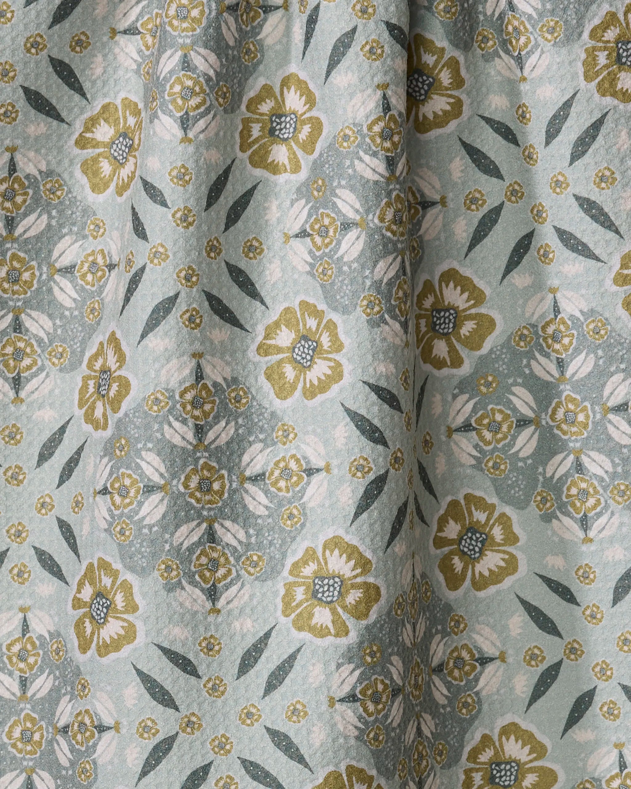 A close-up of Summit Check fabric by Ash Cascade, showing yellow and white flowers with green leaves on a pale blue and white backdrop in a symmetrical, repeating pattern.