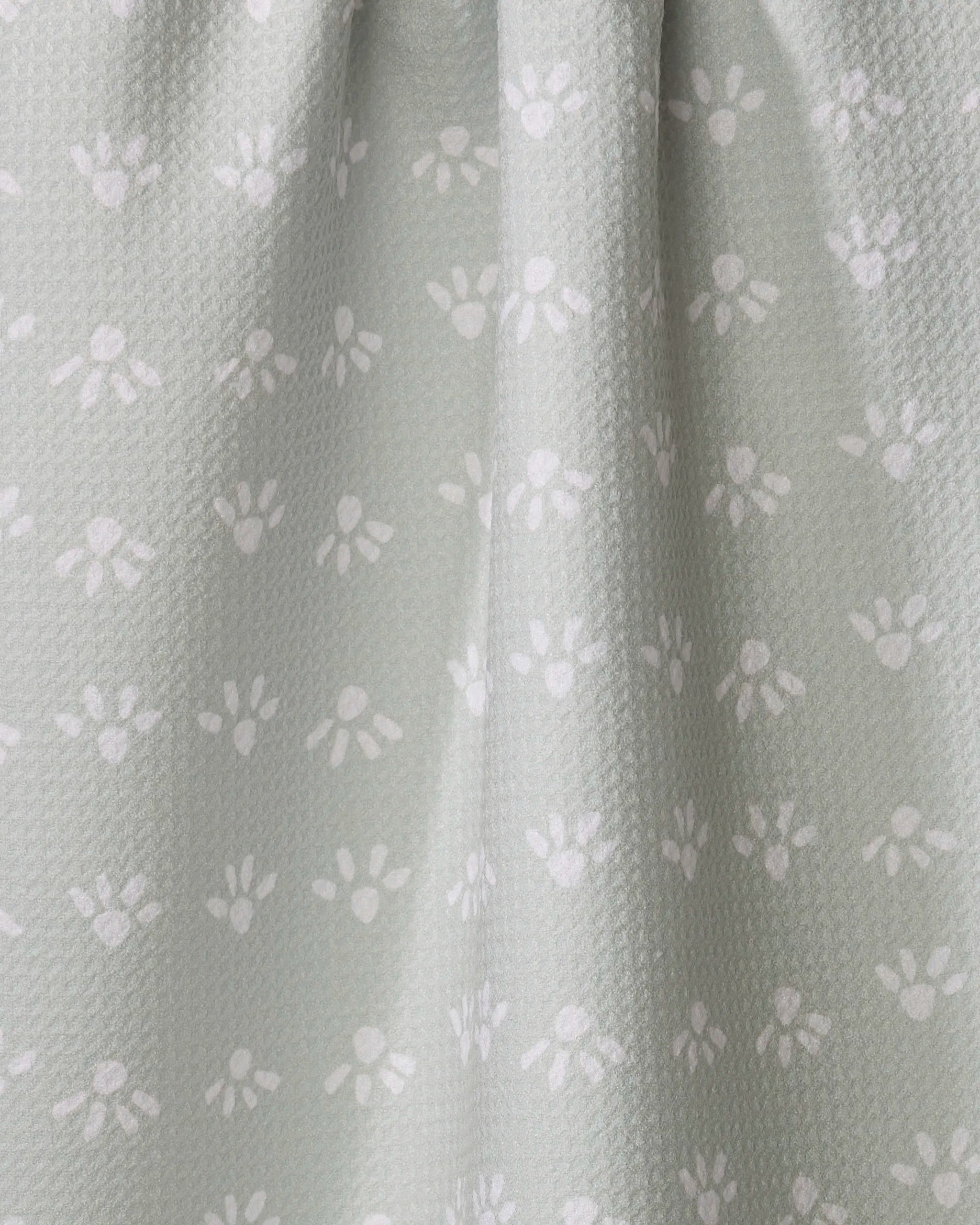 The "Sun Bursts" tea towel by Anee Shah features light gray fabric with a subtle texture, small white paw prints, and gentle vertical folds. Ultra-absorbent and charming, it's perfect for your kitchen.