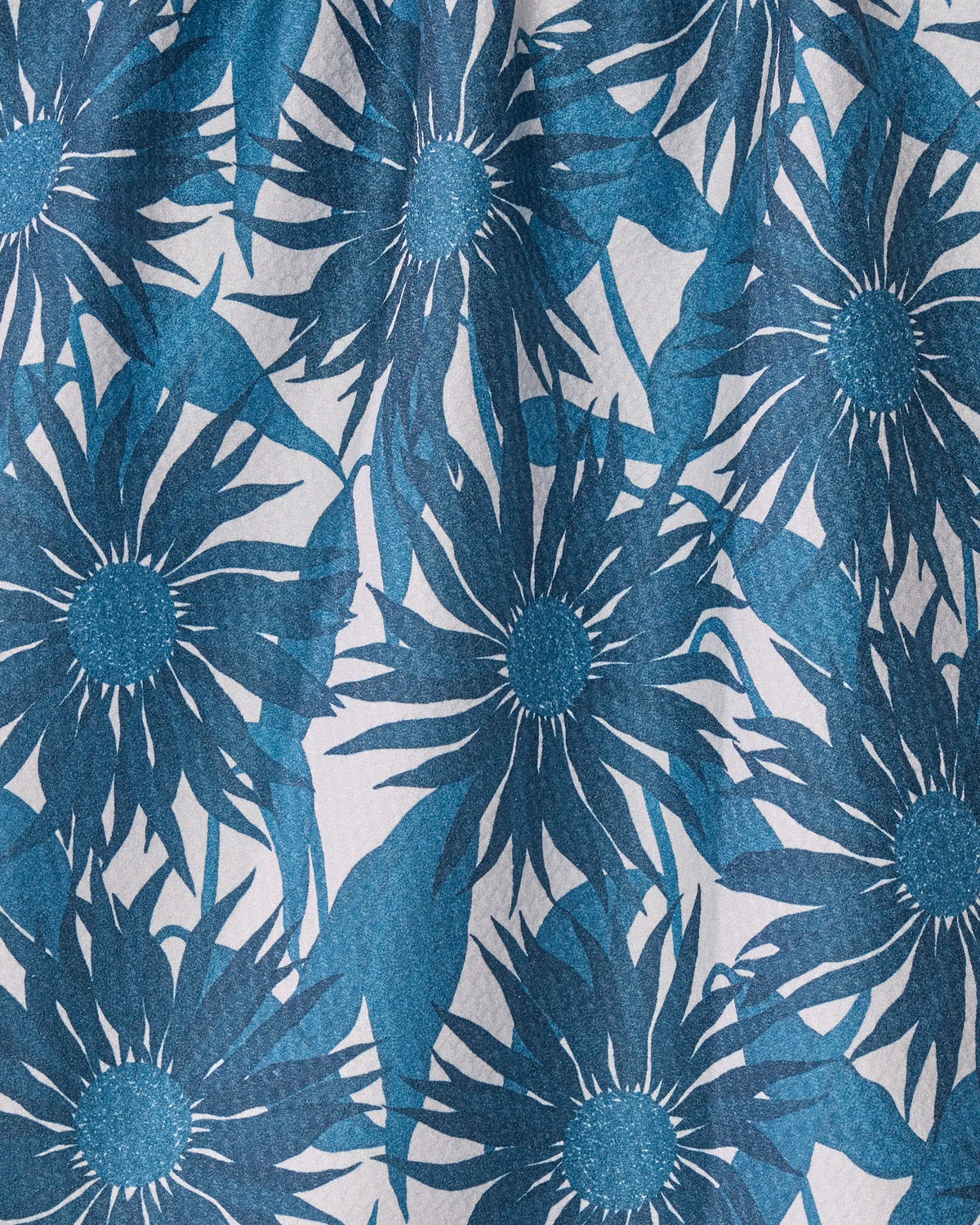 Introducing the Sundara Frost towel from Geometry, featuring a blue floral pattern with large stylized flowers and pointed petals on a light background. The ultra-absorbent design showcases overlapping blooms that span the entire surface, resembling a printed recycled kitchen towel or decorative wallpaper.