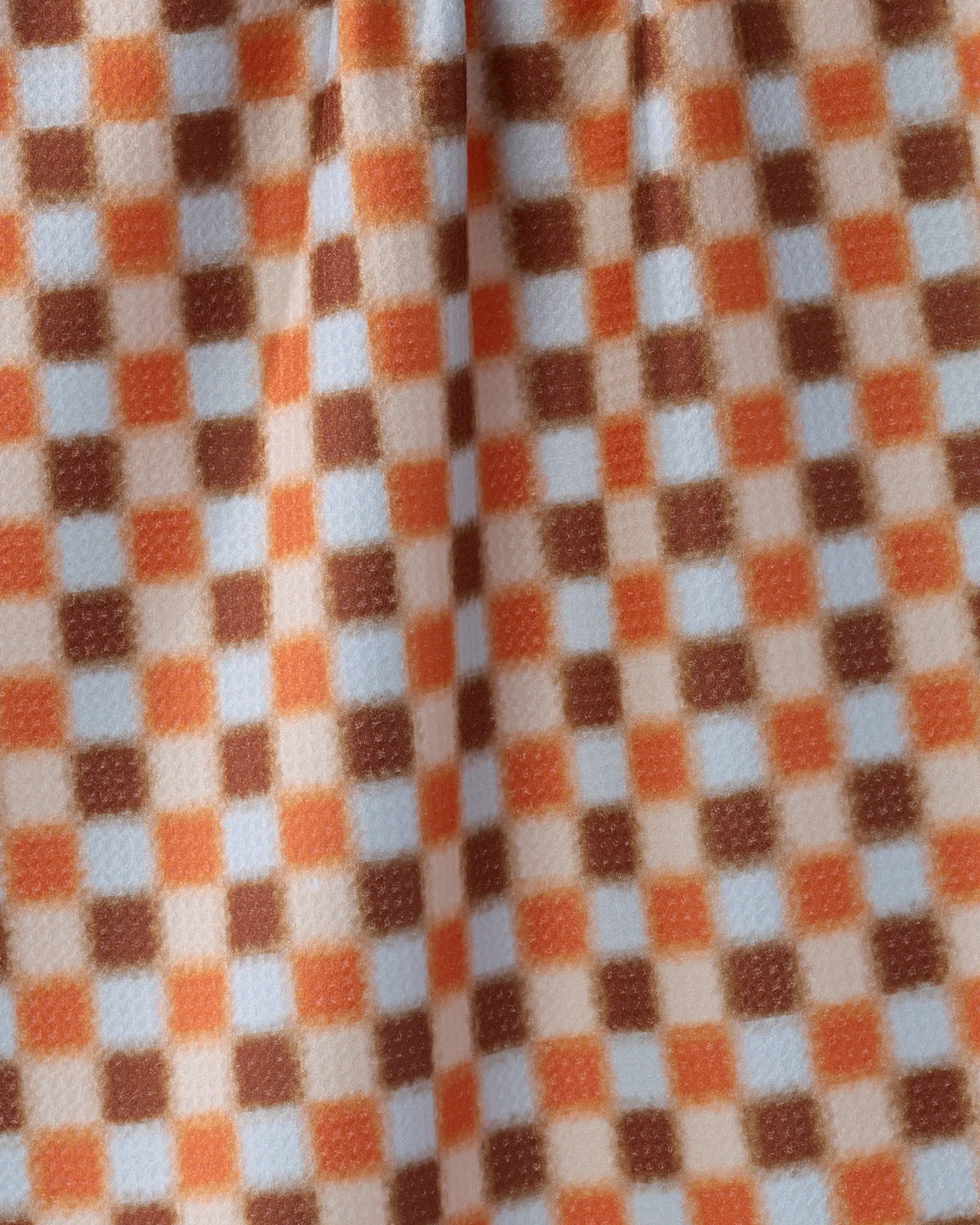 A close-up of the Geometry Sunday Supper tea towel shows its orange, light blue, and brown checkered pattern. Ultra-absorbent and soft with fleece-like folds, it's made from recycled materials and eco-friendly.