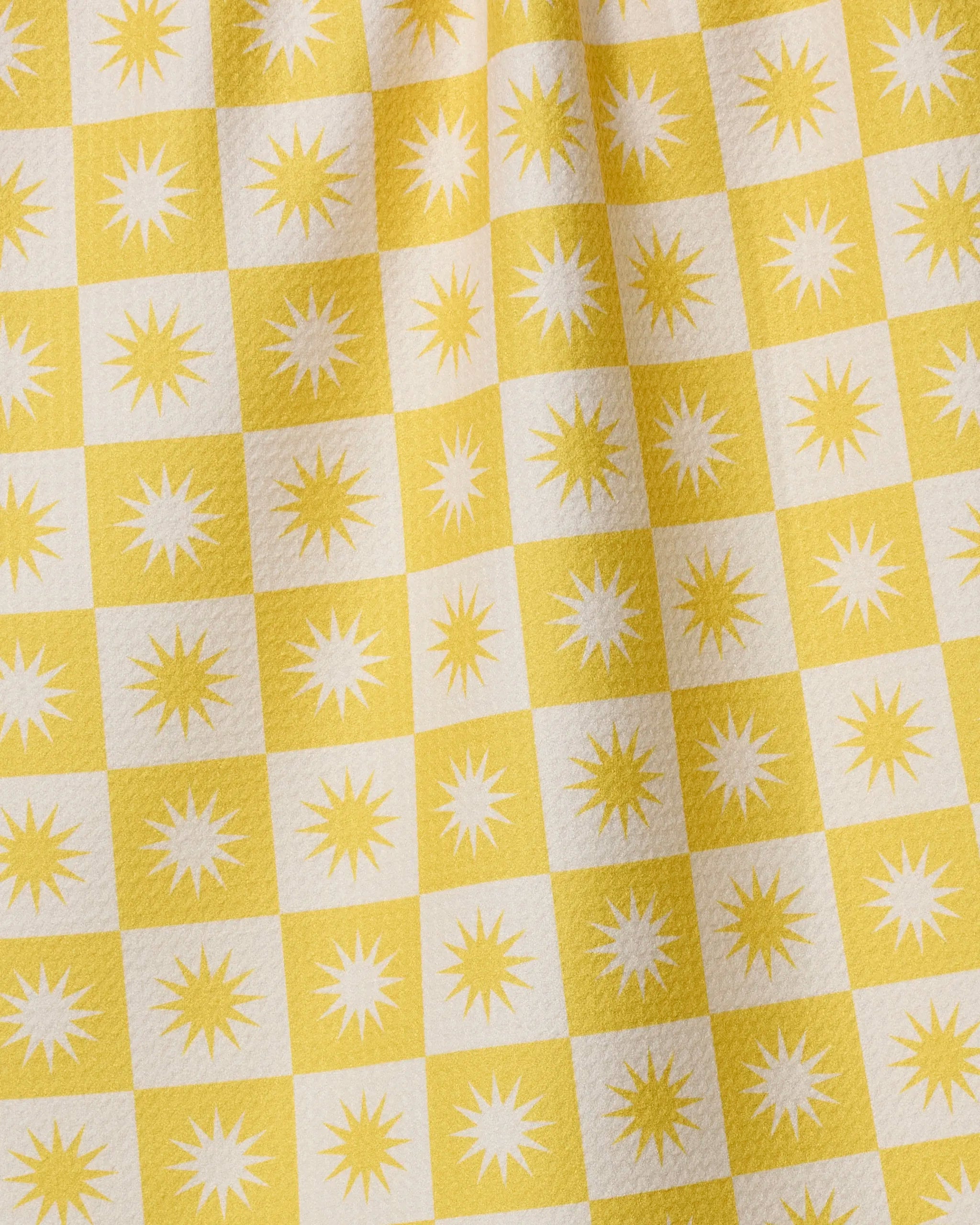The Sundial tea towel by Geometry features yellow and white checks with starbursts, crafted from recycled materials. Its quick-drying, textured surface displays subtle folds.