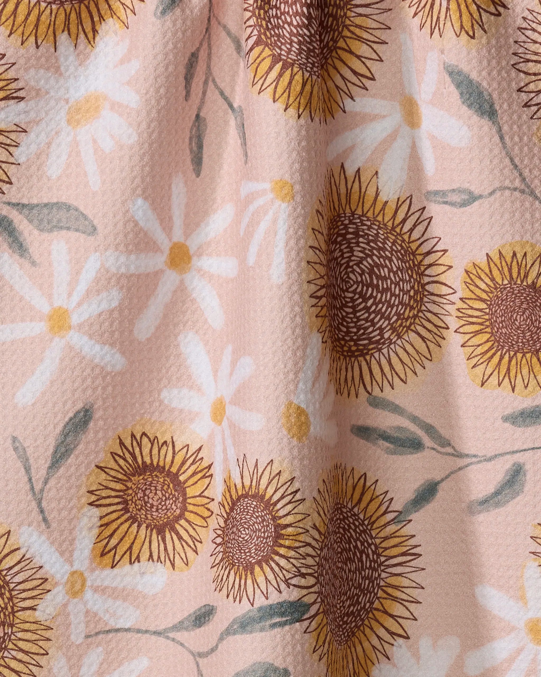 A close-up of Elisabeth Wing's "Sunflowers" recycled kitchen towel, showing a textured fabric with yellow sunflowers, white daisies, and green leaves on a light pink background.