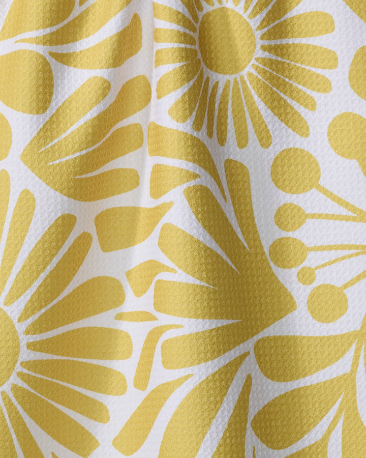Close-up of Lisa Nelson's Sunlit Blooms kitchen towel, made from textured white recycled material and adorned with a yellow abstract floral pattern featuring stylized flowers and radiating petals, with gentle folds and shadows visible.