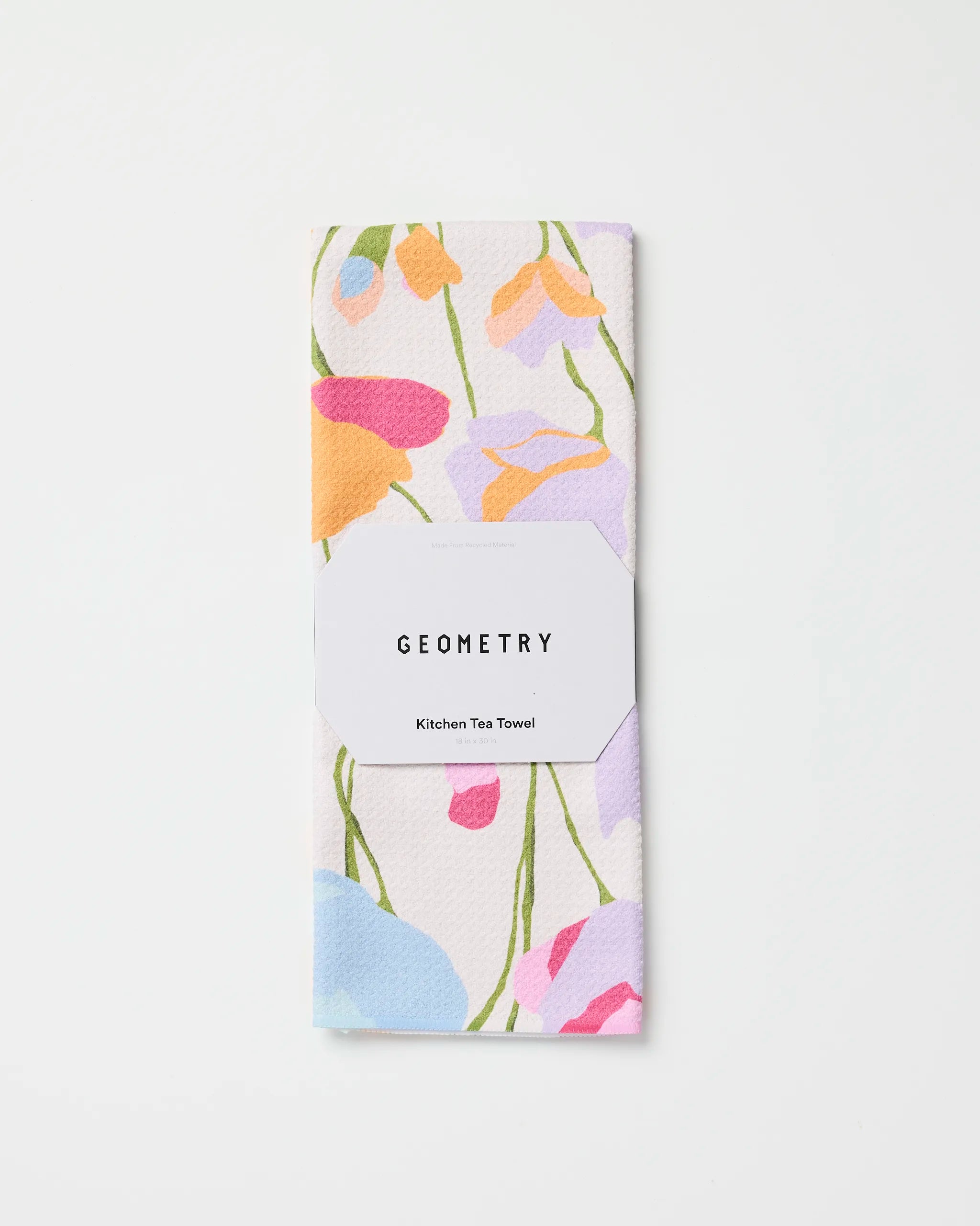 A folded Geometry Sunlit Garden kitchen tea towel featuring a colorful abstract floral design, made from recycled materials, wrapped in a white paper band labeled Geometry Sunlit Garden, shown on a plain white background.