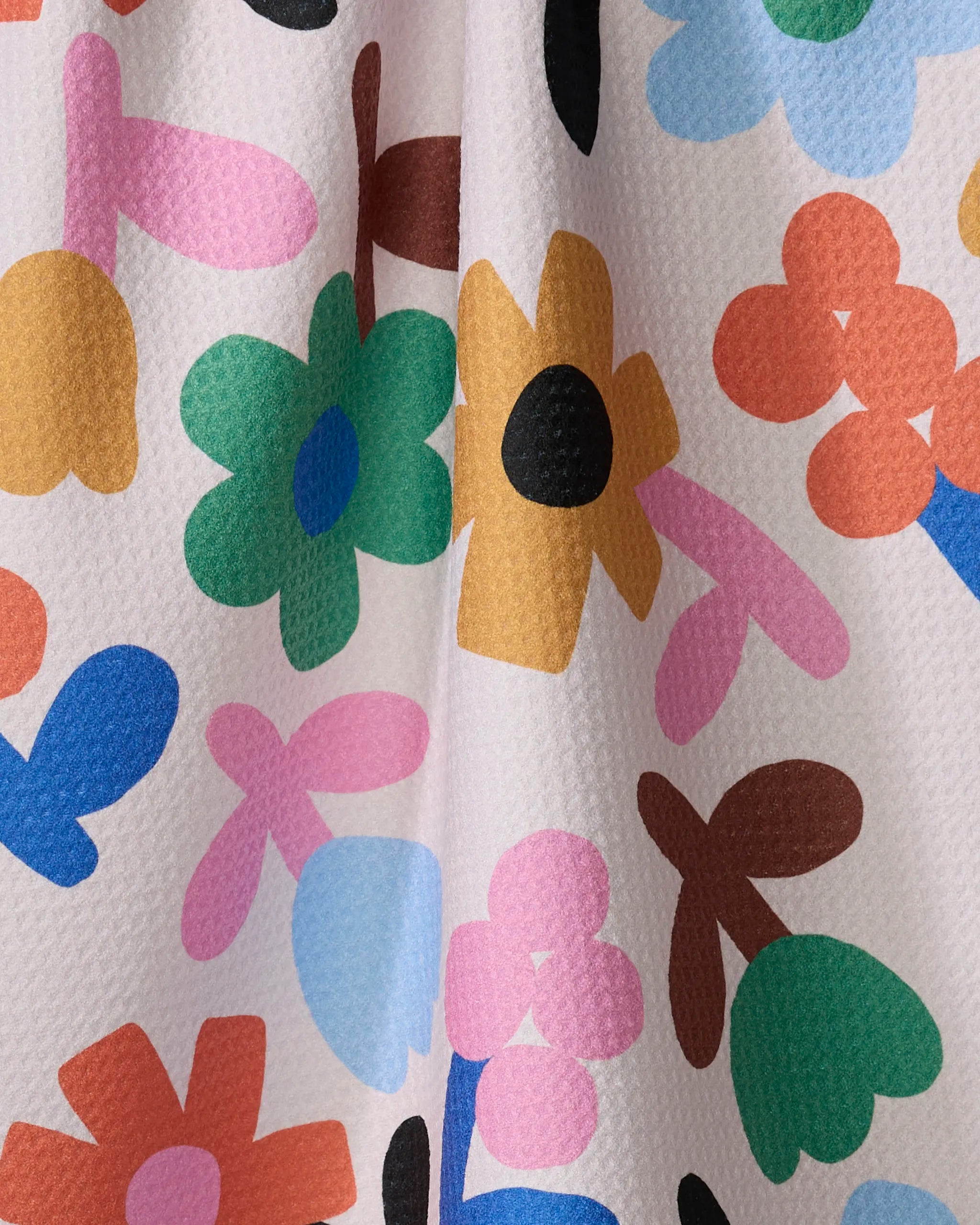 The Sunny Bloom kitchen towel by Jennifer Bouron features a colorful, abstract floral pattern in green, yellow, blue, orange, pink, and black on a textured white eco-friendly fabric.