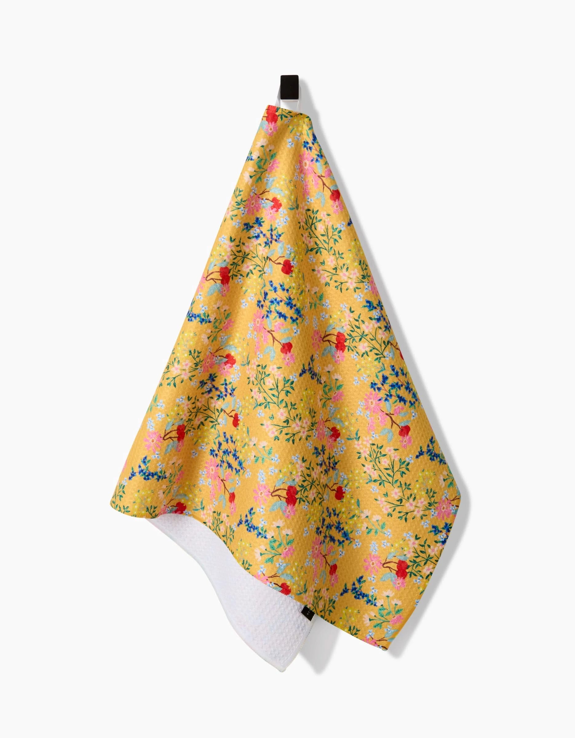 The Sunny Cherry Blossoms Geoweave™ tea towel by Brittany Jepsen features a colorful floral pattern with pink, red, and blue flowers plus green leaves. Made from recycled materials, it hangs from a black hook against a white background.