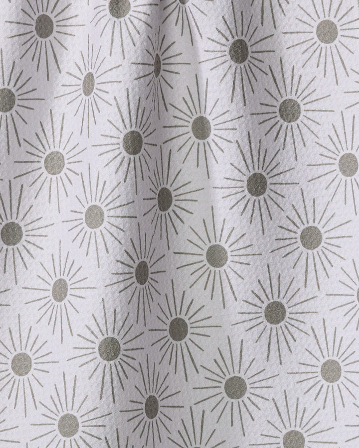 The Hufton Studio "Sunny Geo" tea towel features a white fabric with repeating gray sunburst patterns, each with a solid circle center and radiating lines, draping softly to create gentle folds and shadows.