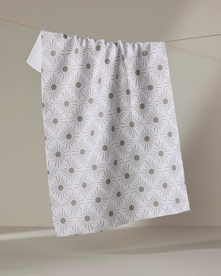 The Hufton Studio Sunny Geo towel, featuring a white ultra-absorbent fabric with a repeating gray geometric sunburst pattern, hangs on a clothesline against a neutral background.