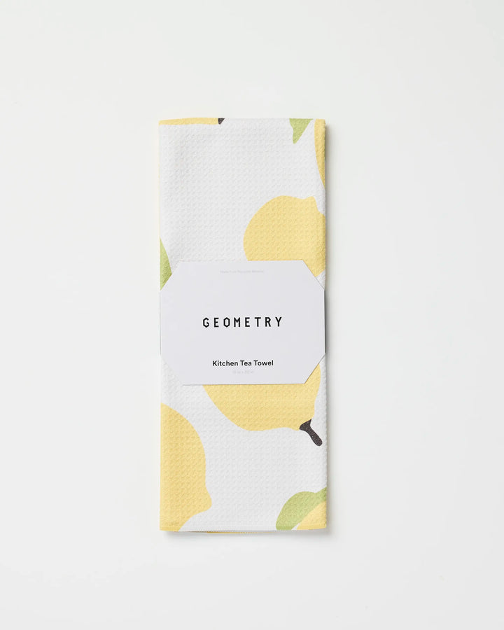 A folded white tea towel with a yellow lemon pattern, called Sunny Lemons by GEOMETRY, made from recycled materials and wrapped in branded packaging, rests on a plain white background.