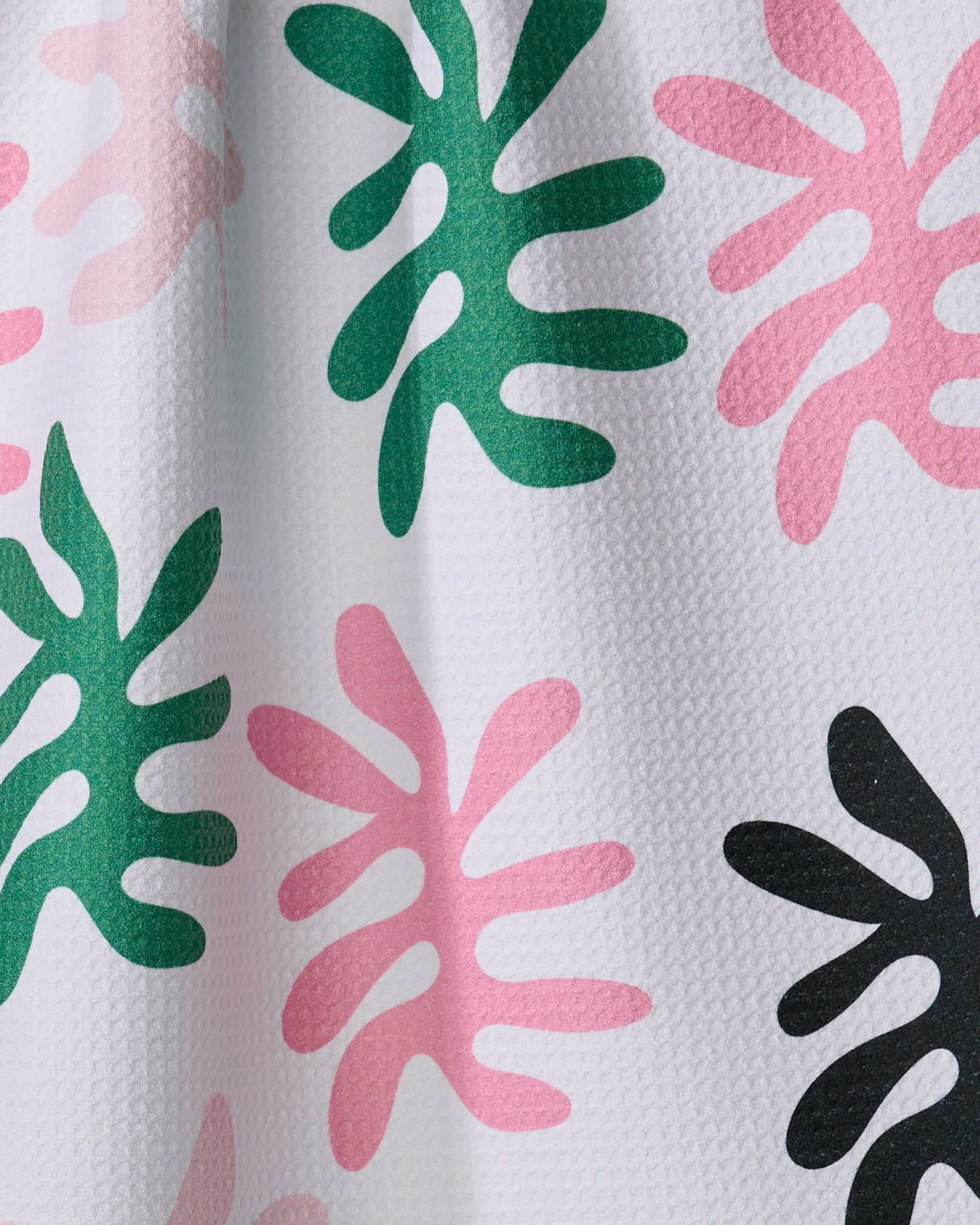 Sunrise by Marina Solodka is a white textured tea towel made from recycled materials, featuring green, pink, and black abstract leaves in a Matisse-inspired cut-out style with rounded shapes scattered across the fabric.