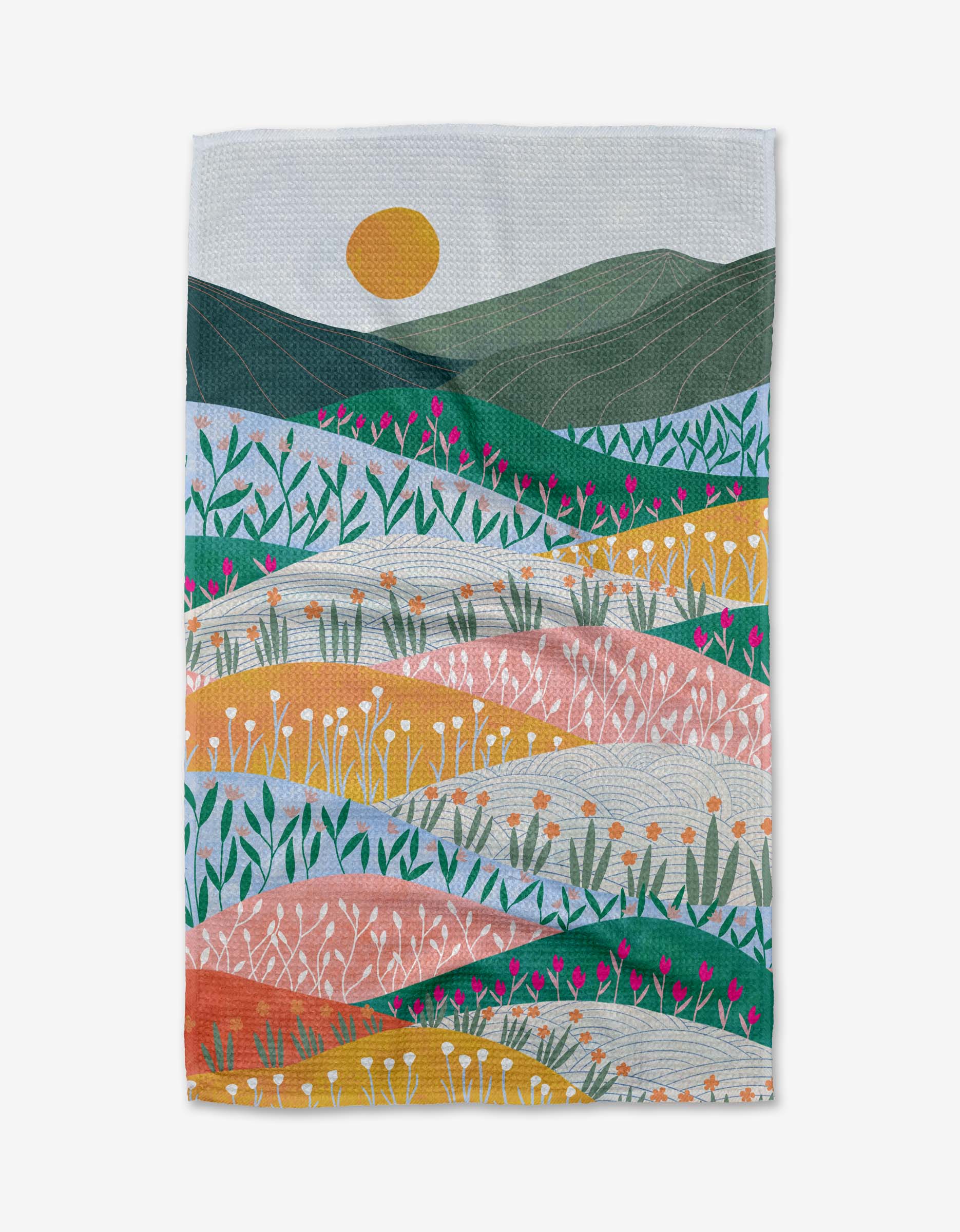 The Sunrise Mountains tea towel by Ceyda Alasar features an abstract landscape with rolling hills, colorful flowers, green mountains, and a yellow sun. Made from ultra-absorbent Geoweave fabric with lively patterns and bold colors.