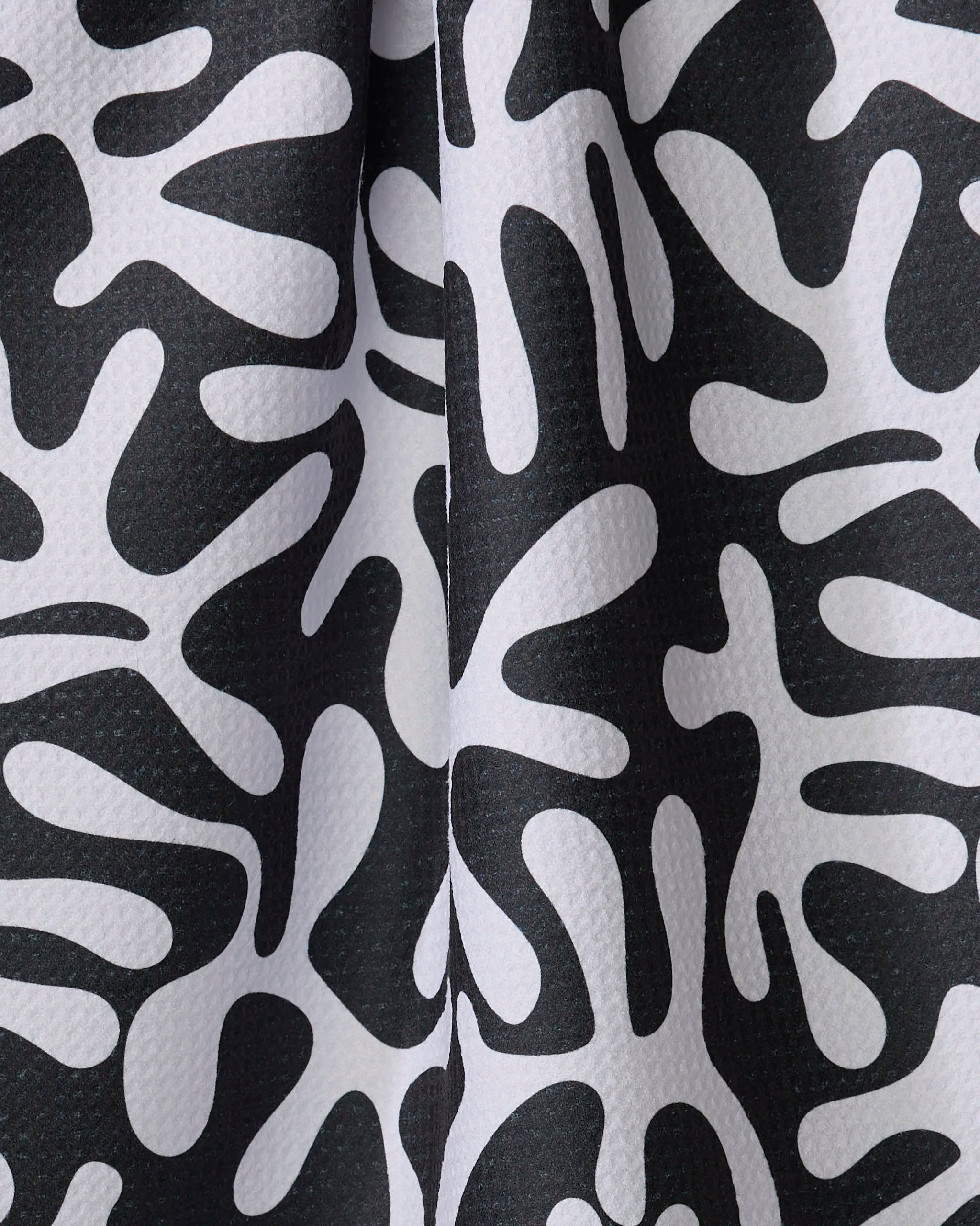 A close-up of Marina Solodka’s Sunset towel shows its black and white abstract pattern, organic coral-like shapes, quick-drying fabric, textured and slightly raised surfaces with visible folds.