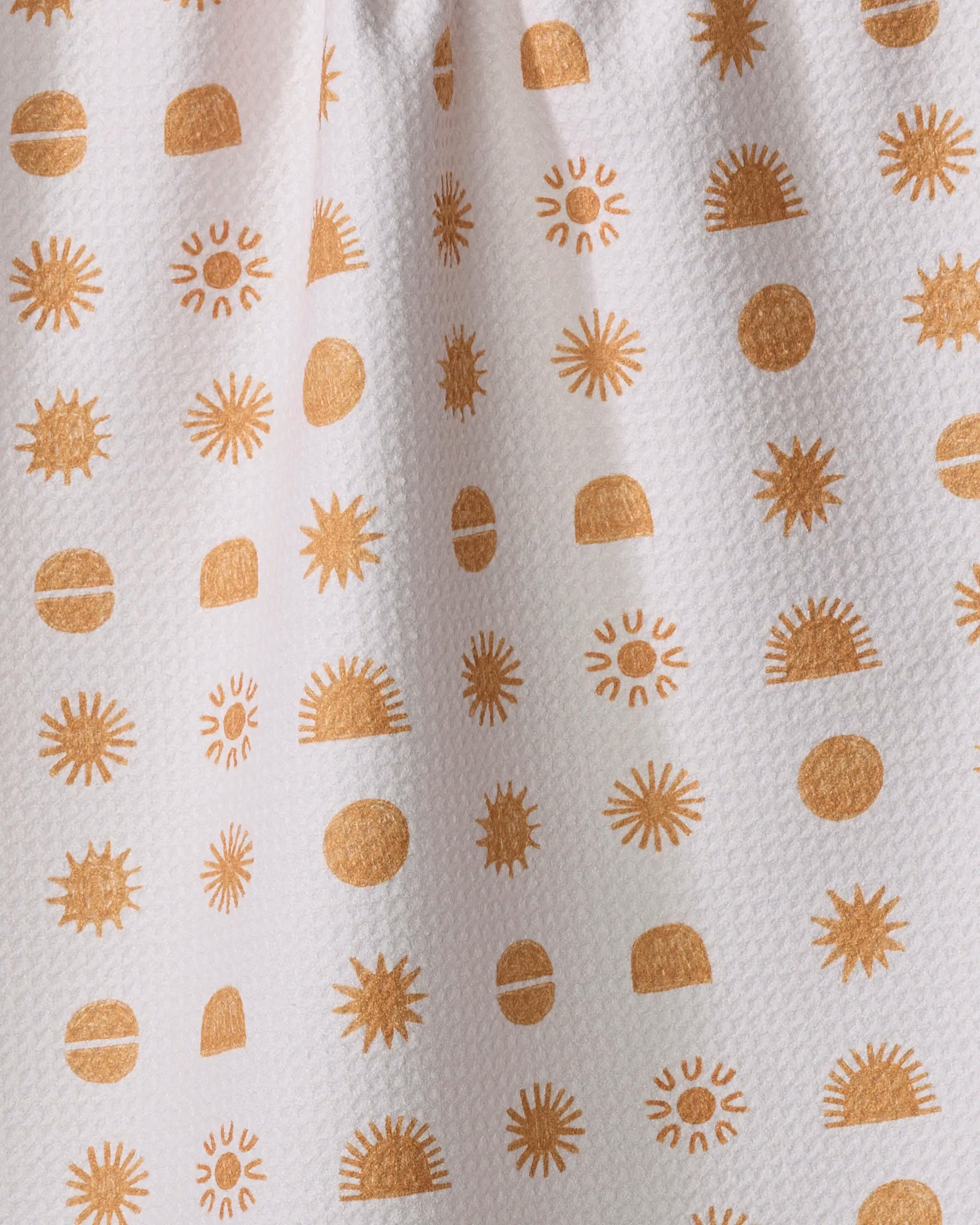 Sunshine by Jen B. Peters is a white recycled kitchen towel with a textured surface, featuring orange sunbursts, half suns, and circles for a cheerful and playful look.