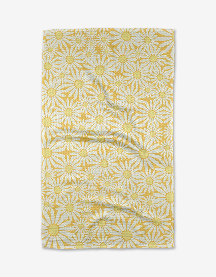 The Rebecca Bobko Sunshine Meadow rectangular cloth, made from ultra-absorbent Geoweave fabric, features yellow and white daisies with large yellow centers on a white background and is shown slightly wrinkled on a white surface.