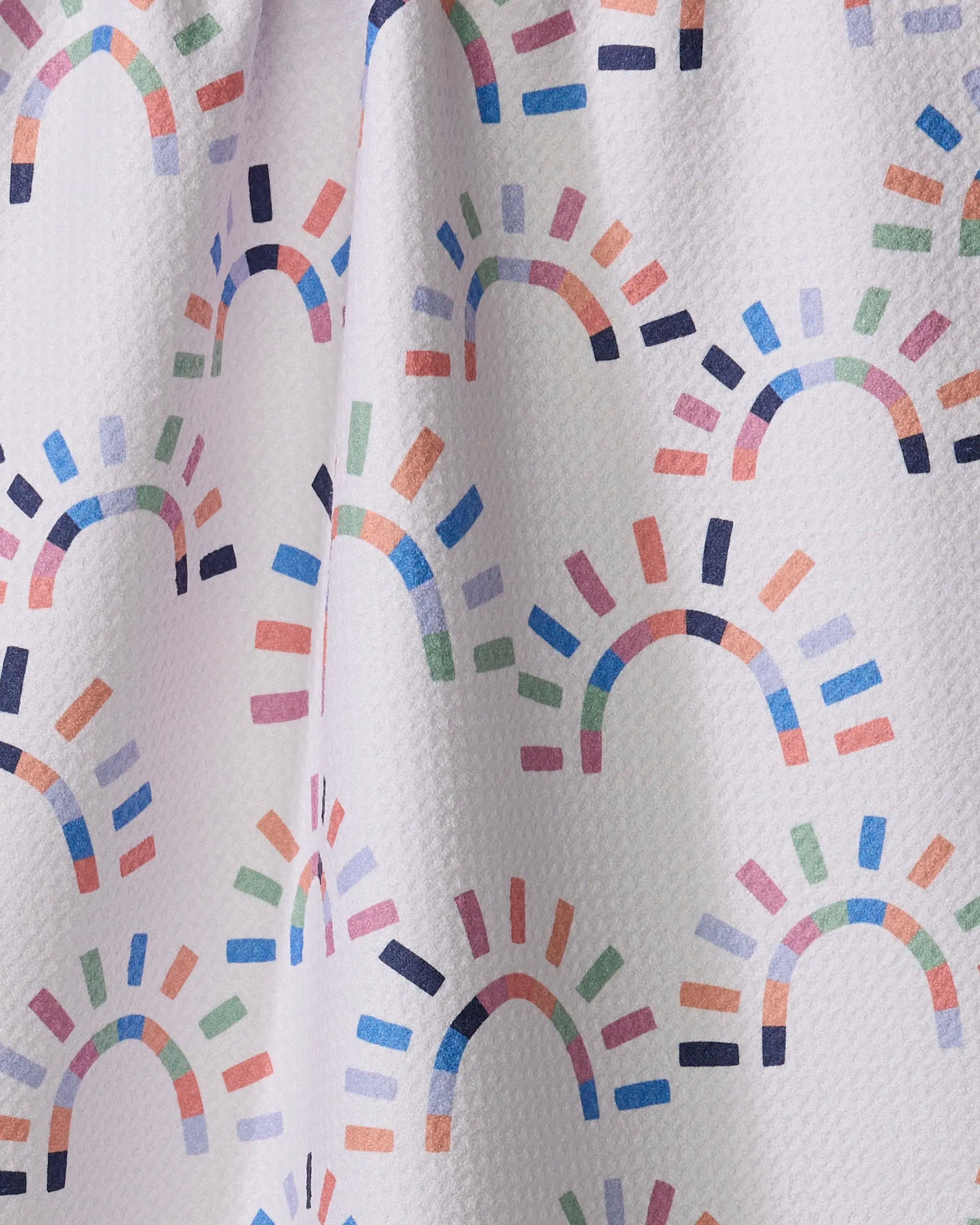 The Sunshine Rainbow kitchen towel by Claire Iglesias features a white textured fabric with colorful semi-circular arches and lines in blue, pink, orange, green, and purple—perfect for brightening up your kitchen.