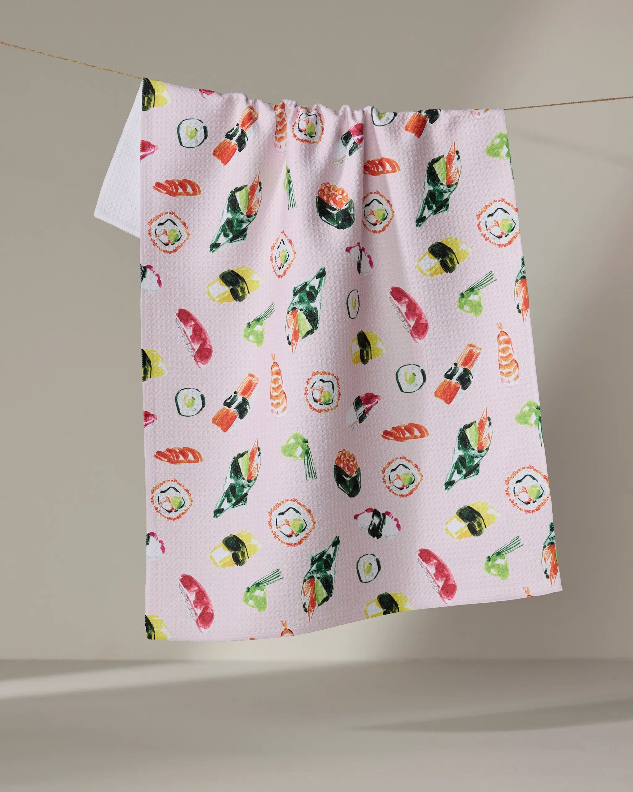 The "Sushi in Tokyo" kitchen towel by Travel Write Draw (Meagan Morrison) features colorful sushi illustrations and hangs against a neutral background.