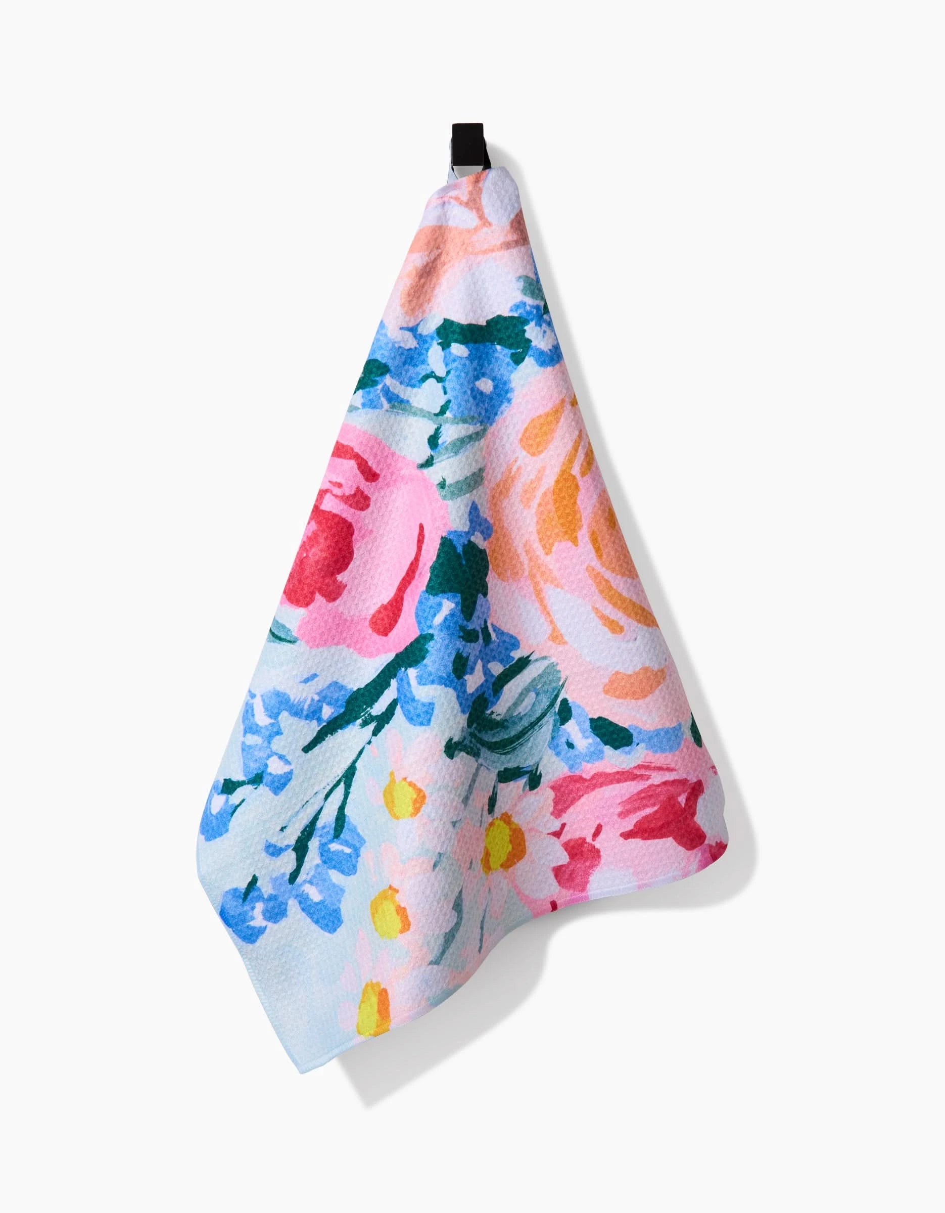 The Suzzy tea towel by Ania Zwara Art features a vibrant floral design in pink, blue, yellow, and green on soft Geoweave fabric for superior absorbency, and hangs from a black loop against a white background.