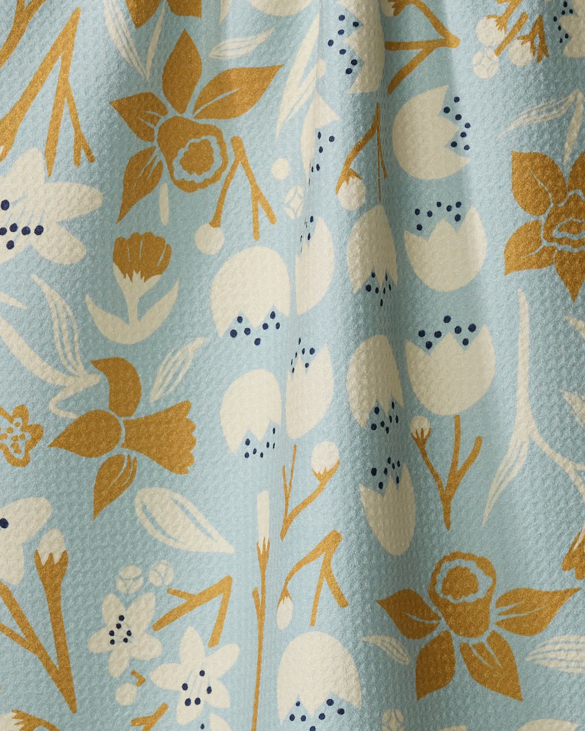 The "Swedish Cherry Blossoms" tea towel by Elisabeth Wing features a light blue background with mustard yellow, white, and black floral patterns. Made from recycled materials, it has a slightly textured finish.