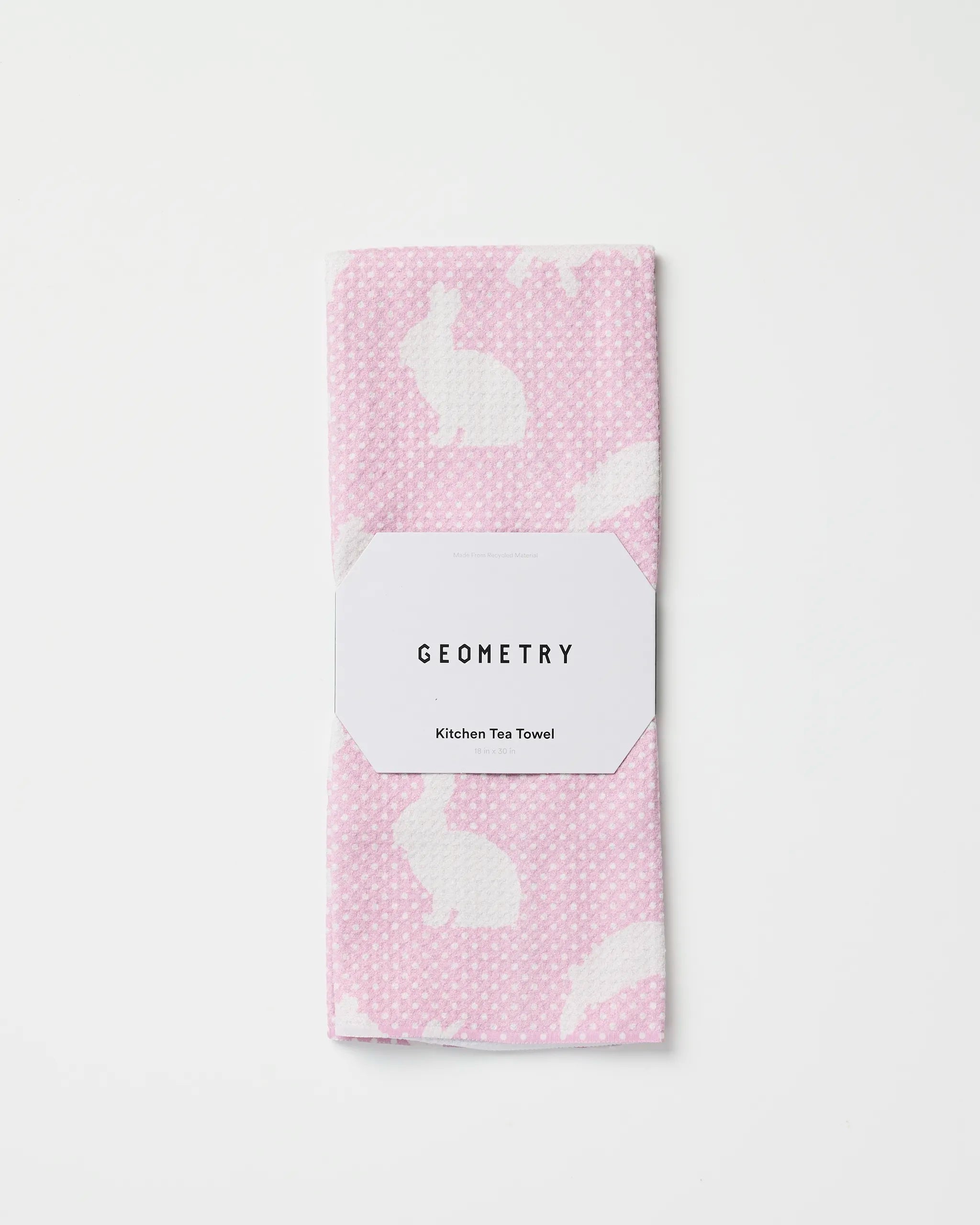 The Geometry Sweet Bunny kitchen tea towel, made from quick-drying recycled materials, features pink fabric with white polka dots and bunny silhouettes. It is folded and wrapped with a GEOMETRY label on a plain white background.