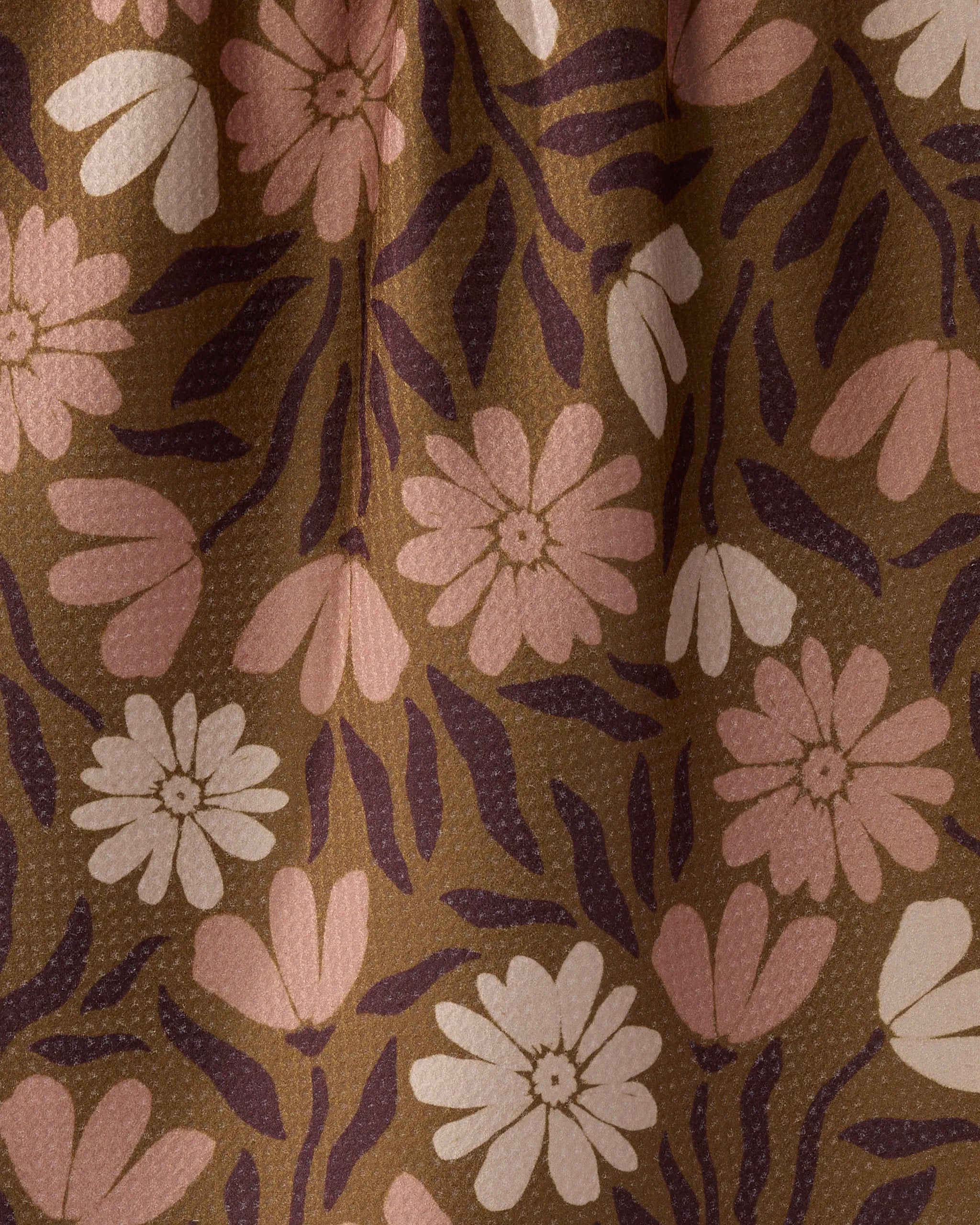 A close-up of Geometry’s Sweet Meadowlane tea towel, made from recycled materials. It features brown fabric with light pink, cream, and purple stylized flowers and leaves, a subtle dotted texture, and appears slightly folded.