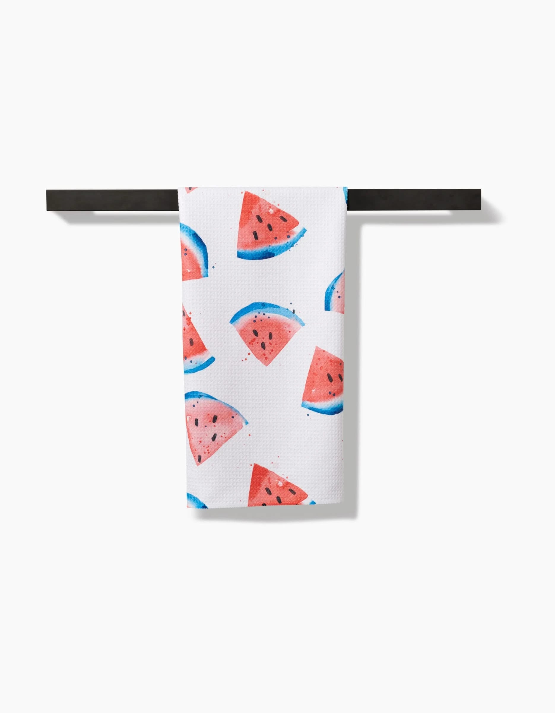 The Sweet Slice Of July tea towel, made from recycled materials, displays a vibrant watermelon pattern and hangs neatly folded over a black rod against a plain white background.