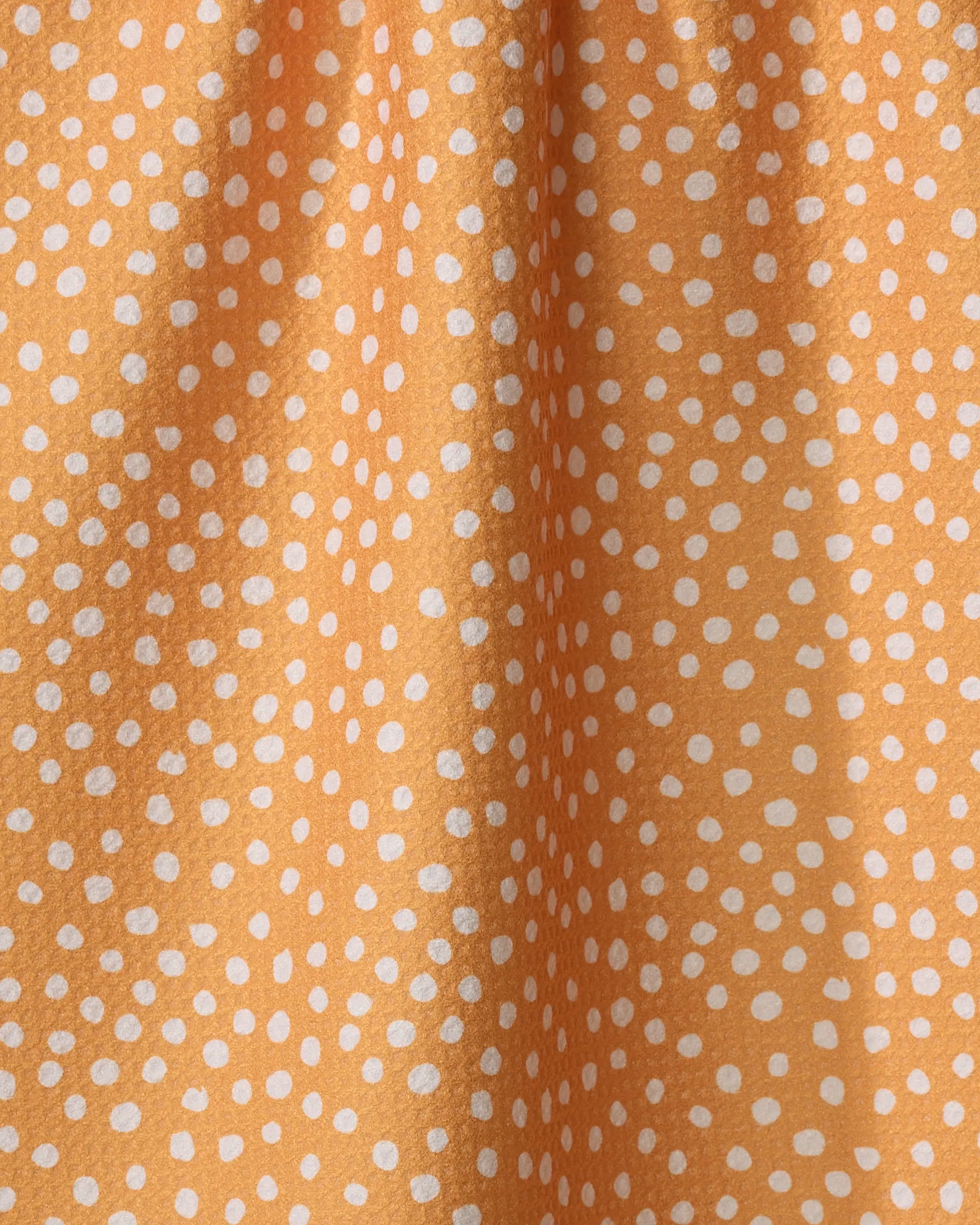 Close-up of Purely Kaylie’s Sweet Sunshine tea towel, an eco-friendly fabric with irregular white dots on a warm orange background. Abstract and playful, the material is softly gathered at the top.