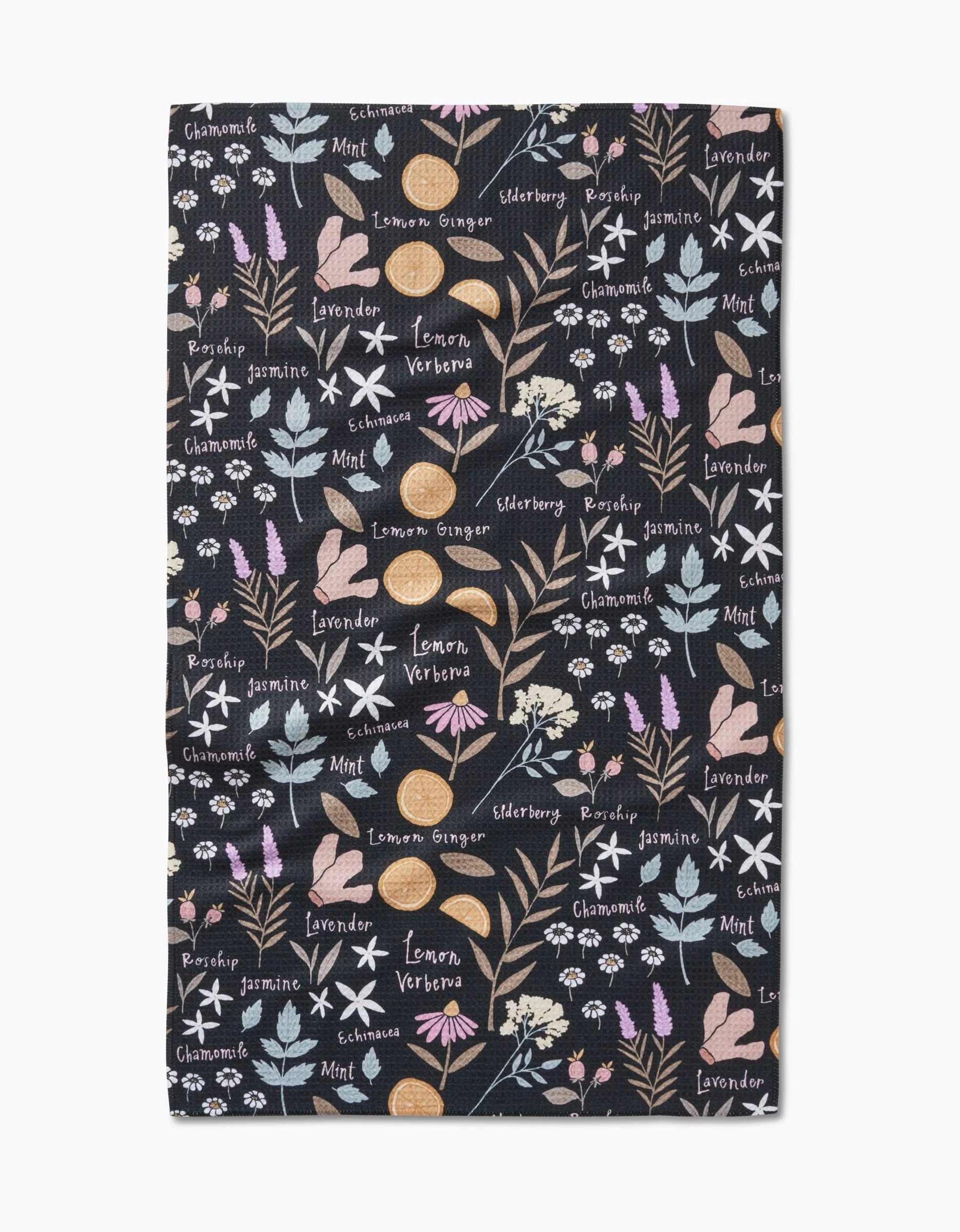 The Sweet Tea rectangular tea towel by Janna Sue Design features a dark recycled backdrop with pastel illustrations and white names of herbs and flowers—like chamomile, lavender, mint, lemon, ginger, and elderberry.