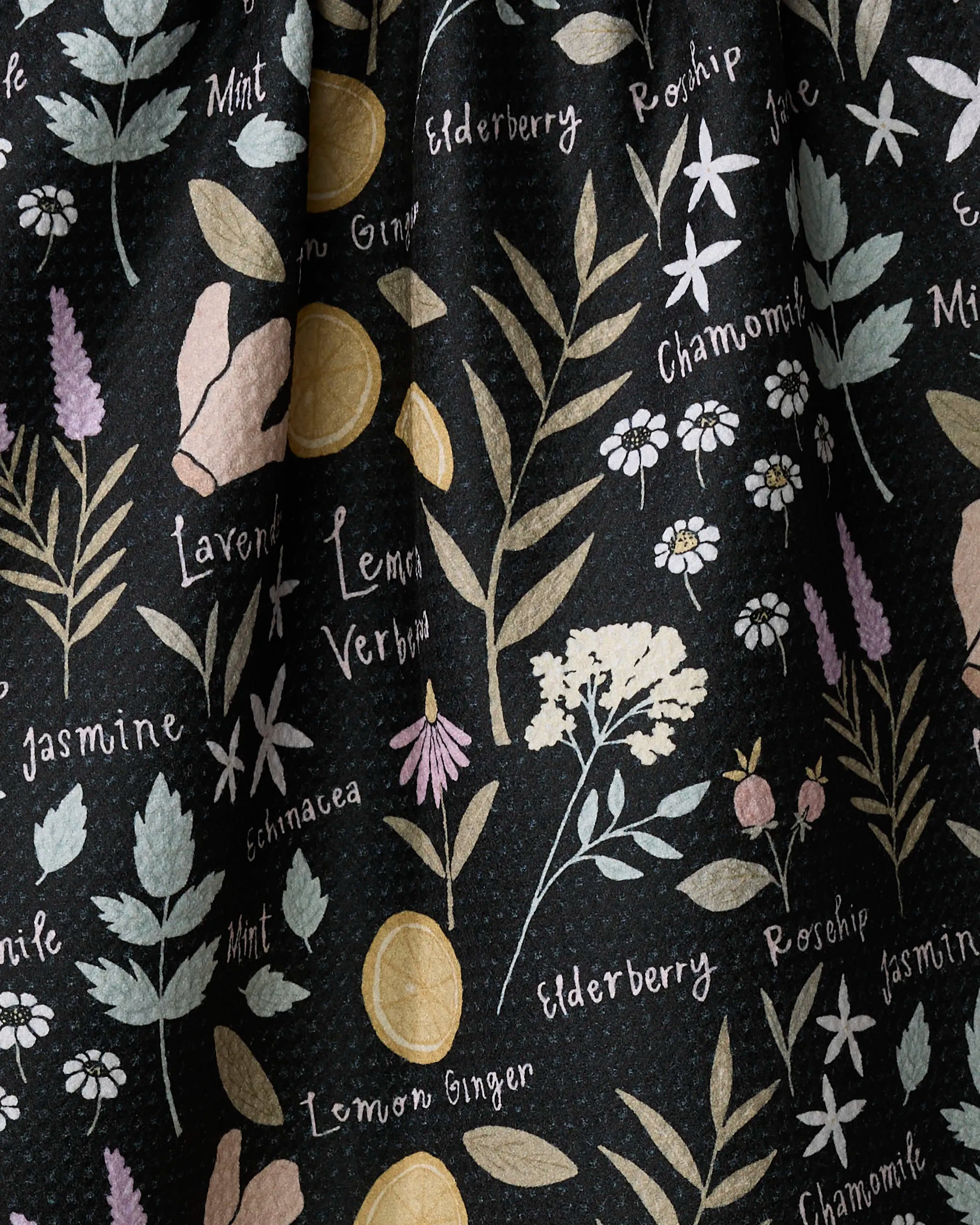 The "Sweet Tea" towel by Janna Sue Design is ultra-absorbent and features a botanical print with illustrated herbs and flowers—lavender, mint, jasmine, elderberry, chamomile, and rosehip—with names in cursive on black.