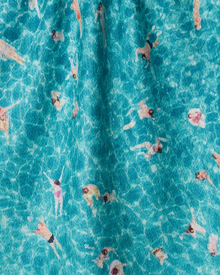 An aerial view of a lively crowd swimming in bright blue water mirrors the vibrant, textured patterns of the "Swimming Crowd" recycled kitchen towel by Geometry.