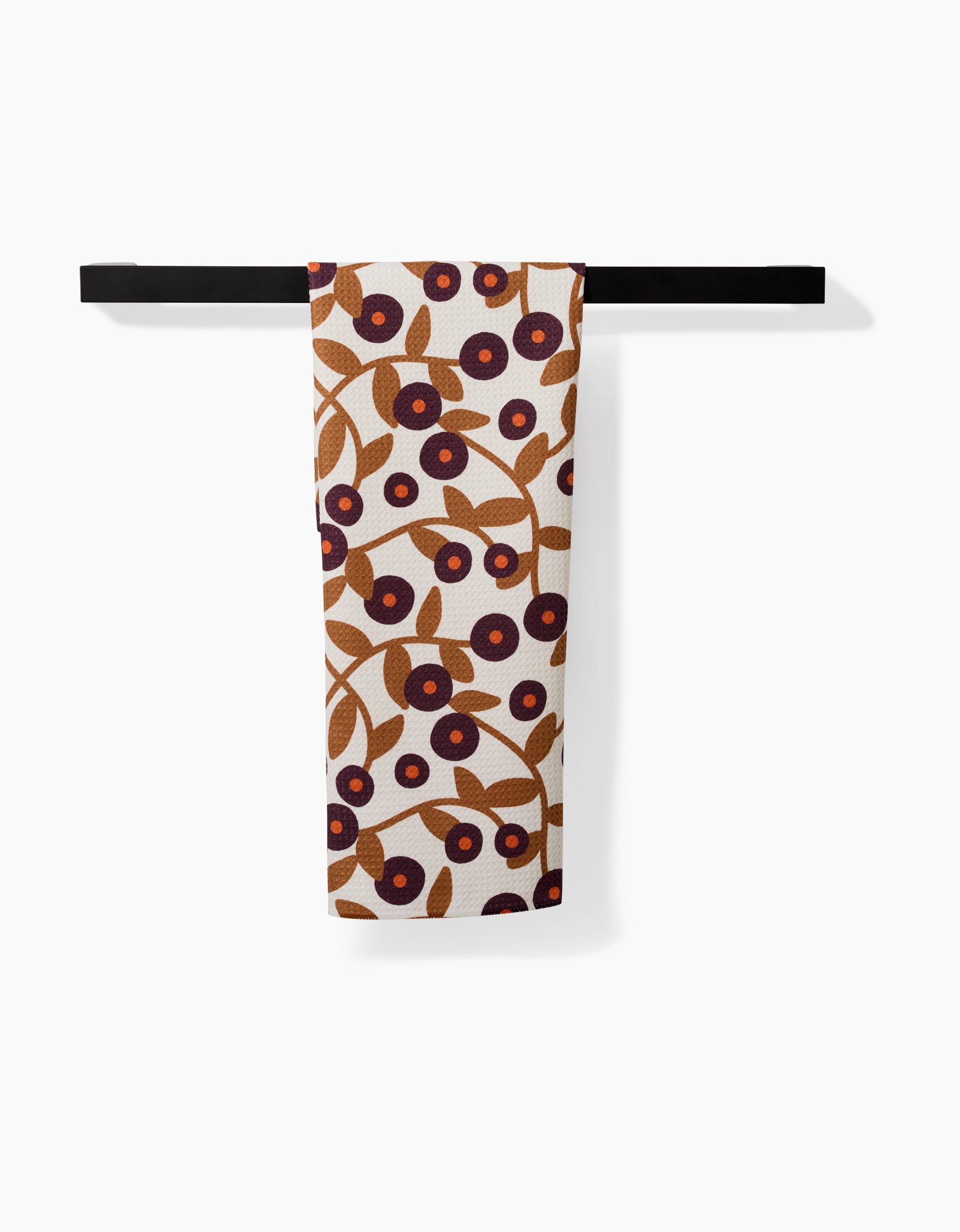 The Swirling Vines tea towel by Lizzie Clark, with a brown and dark red berry and leaf design, dries quickly and hangs neatly on a black towel bar against a plain white background.