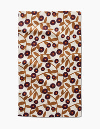 The Lizzie Clark Swirling Vines tea towel is rectangular, made from recycled materials, and features brown branches with leaves and purple and red circular flowers on a cream background.