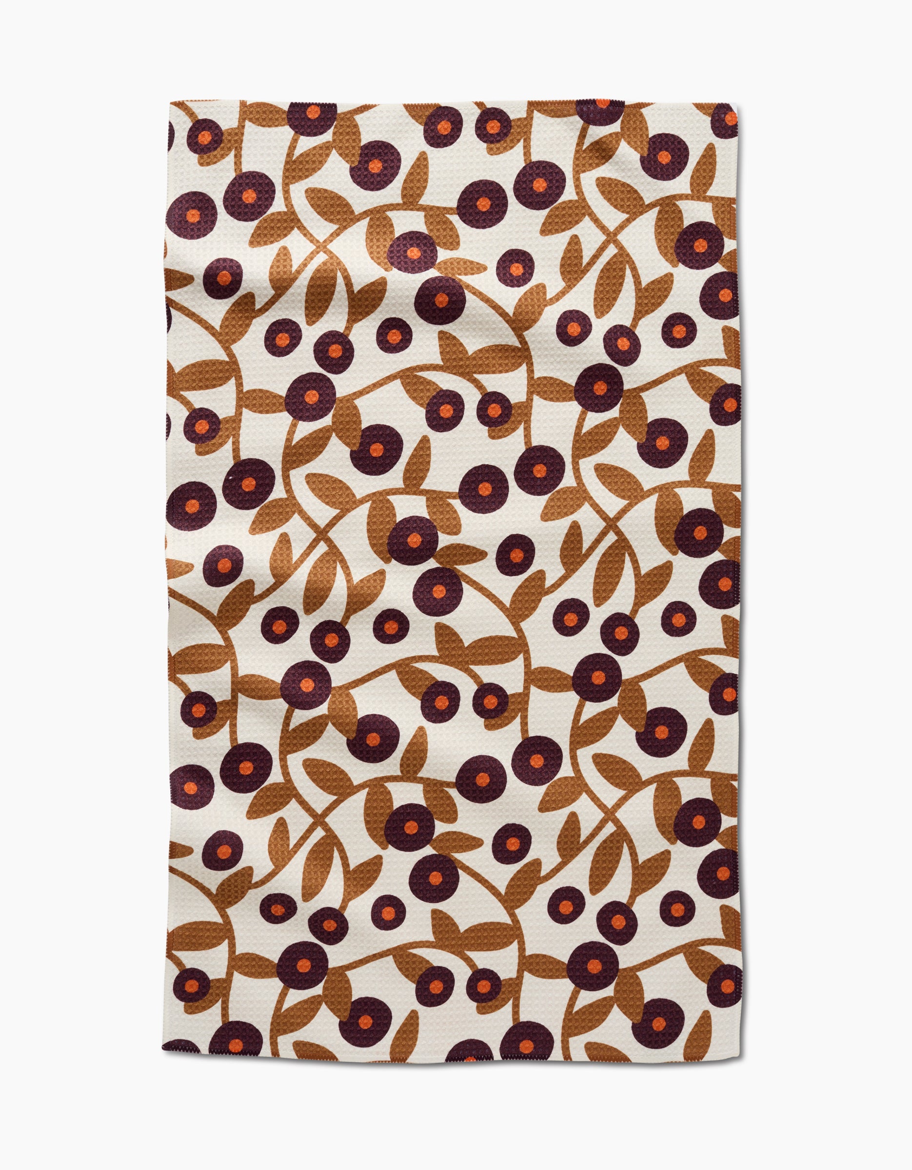 The Lizzie Clark Swirling Vines tea towel is rectangular, made from recycled materials, and features brown branches with leaves and purple and red circular flowers on a cream background.