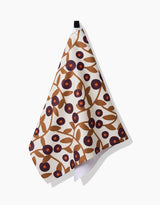 The Swirling Vines tea towel by Lizzie Clark features brown branches, leaves, and clusters of dark red and black berries on white. Made from quick-drying recycled materials, it hangs from a black loop against a white background.