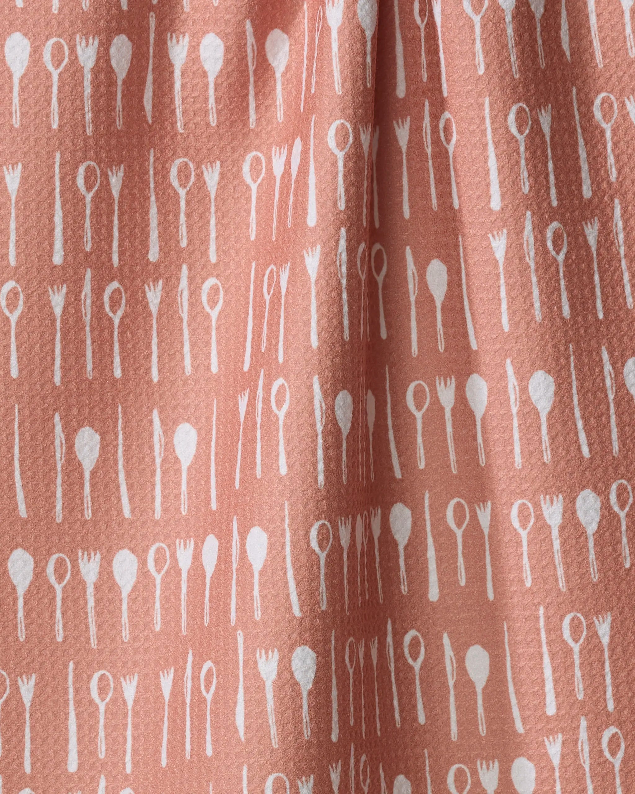 Anee Shah’s Tableware tea towel features a textured pink design with a white kitchen utensil pattern—forks, spoons, knives, and spatulas—crafted from recycled materials.