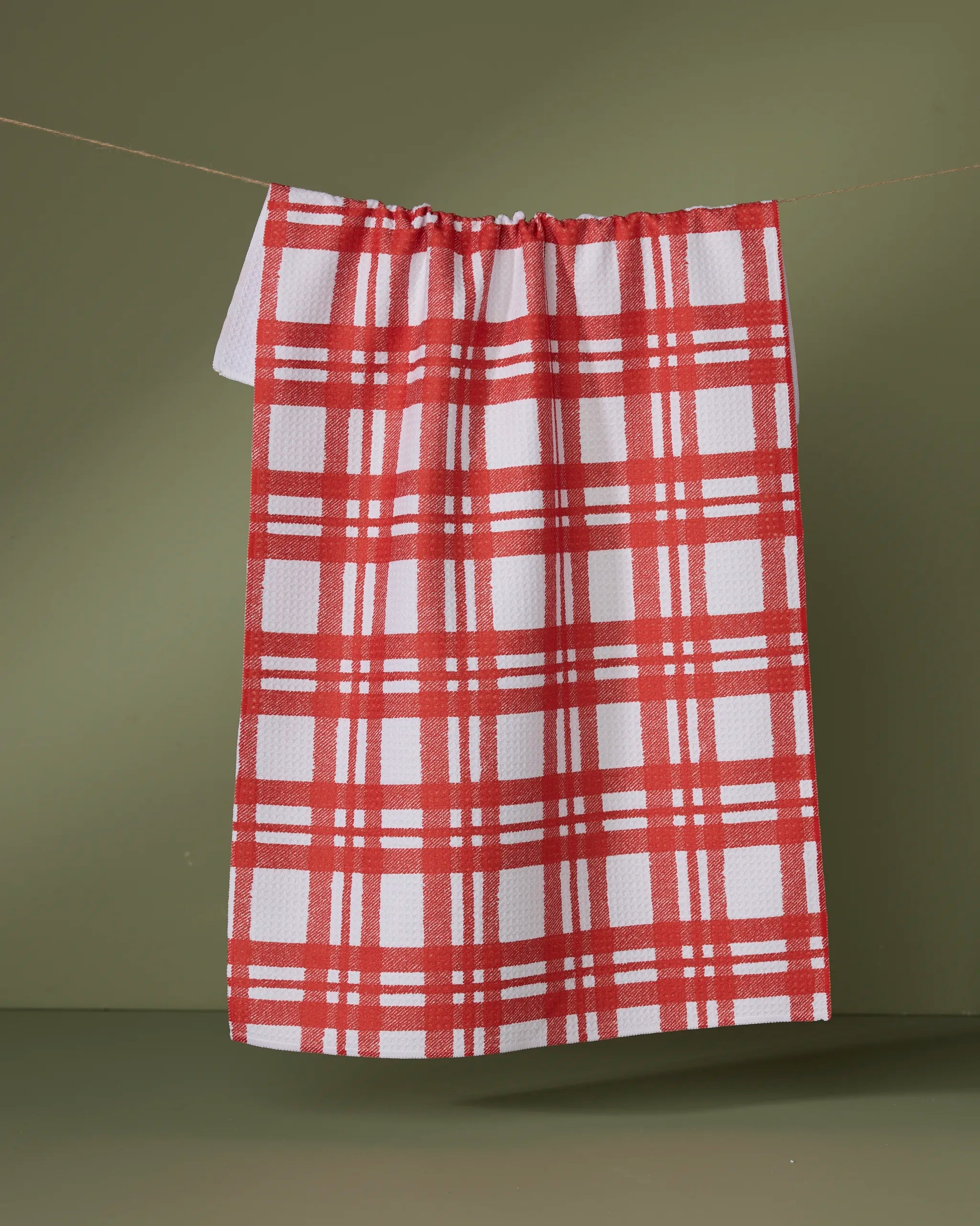 The Geometry Tartan kitchen tea towel hangs on a string against a plain olive green background.