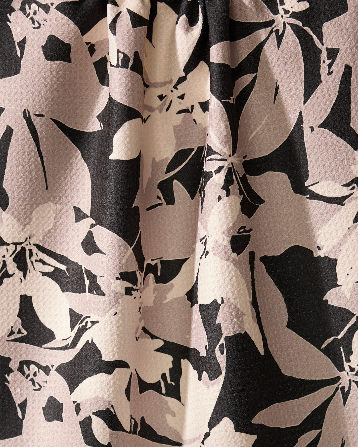 Close-up of Geometrys Tawny recycled kitchen towel featuring a textured surface with overlapping abstract black and pale pink floral patterns and soft, blurred lines.