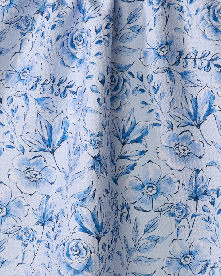 The Sara Mari "Tea Set Blossoms" quick-drying towel features a blue and white hand-drawn floral pattern with roses and leaves on a light, textured background—perfect as a stylish kitchen or tea towel.