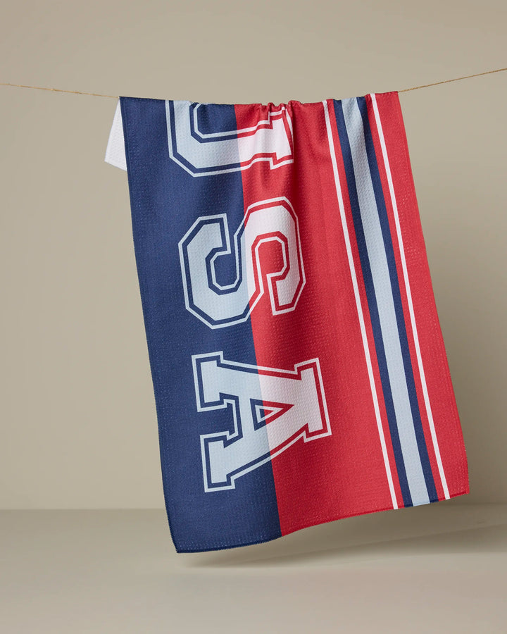 The Geometry Team USA tea towel hangs on a line, showcasing bold blue and red stripes, white and blue lines, and the large white letters "USA" across its ultra-absorbent fabric.